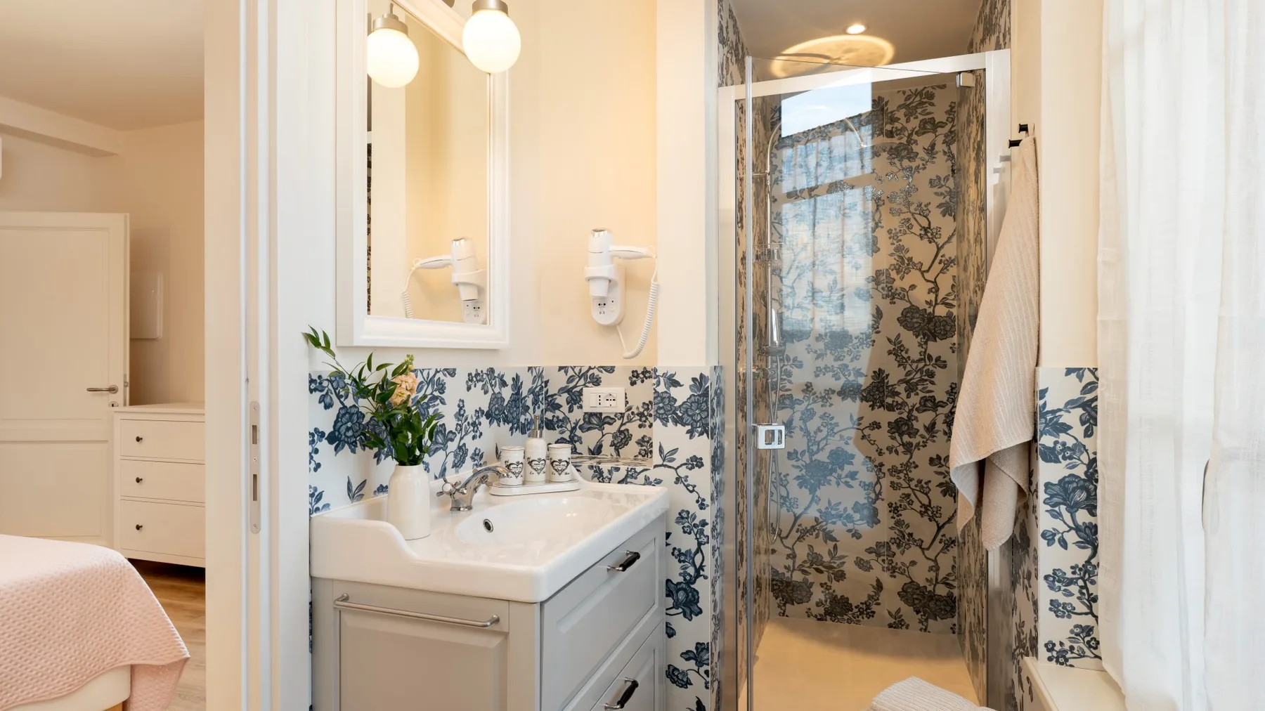 Un baño con lavabo, azulejos florales y una ducha de cristal.