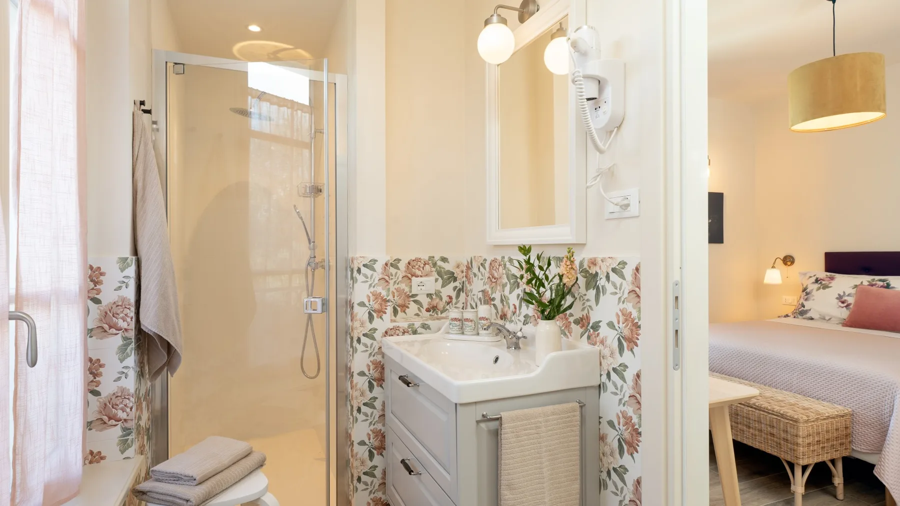 Un baño luminoso con ducha de vidrio, lavabo y azulejos florales.