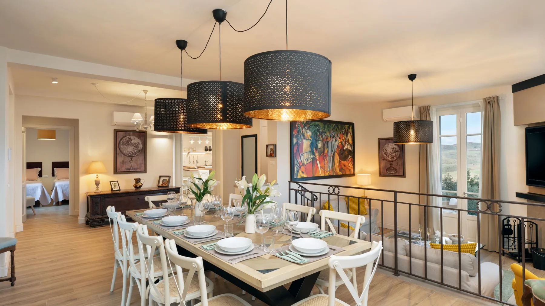 Comedor con una mesa puesta, lámparas colgantes y arte colorido en la pared.