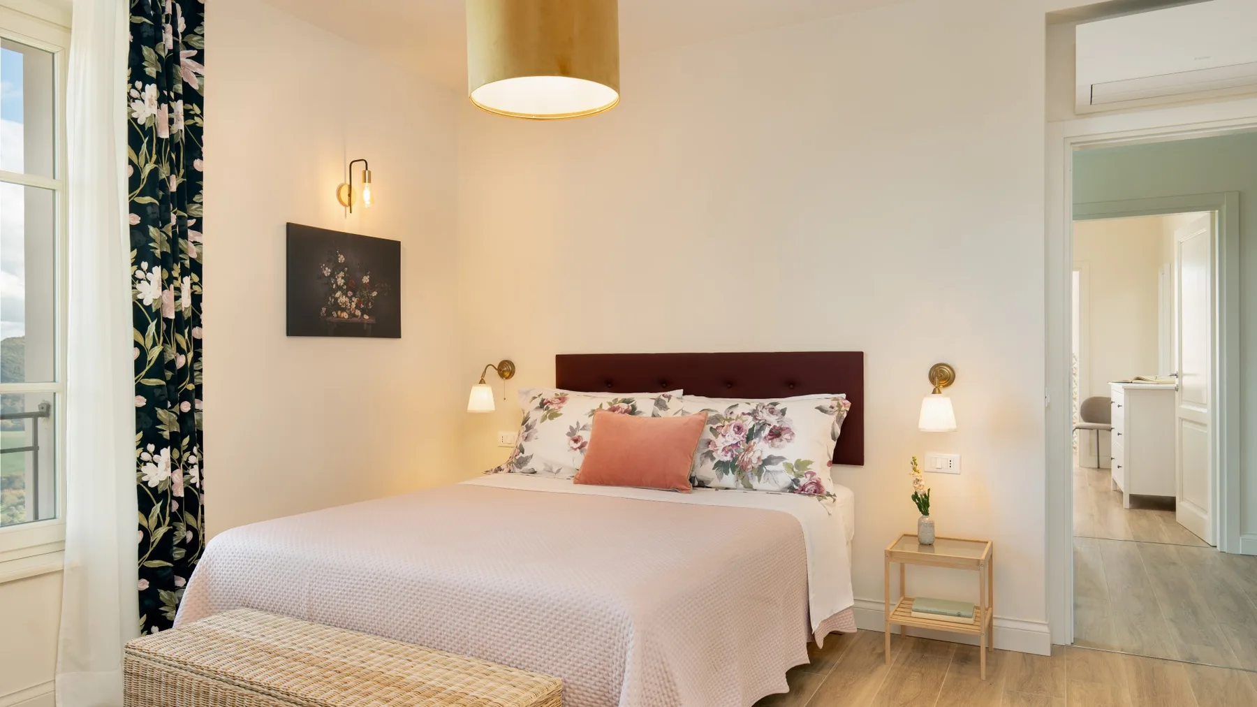 Un dormitorio con una cama vestida con ropa de cama clara y almohadas florales.