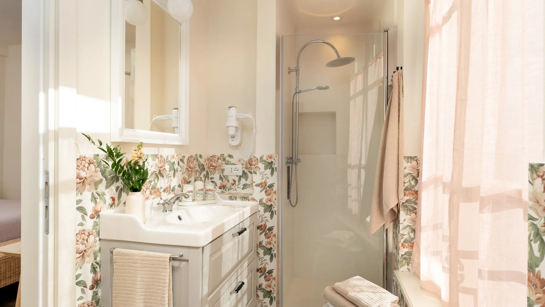 Un baño luminoso con lavabo, azulejos florales y una ducha de vidrio.
