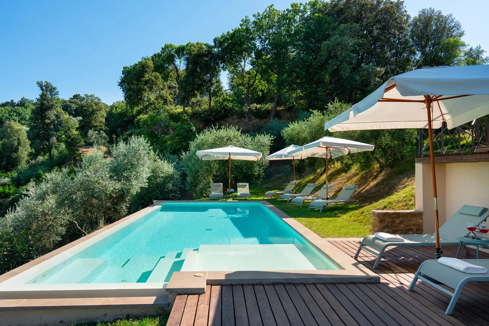 Una piscina al aire libre está rodeada de asientos reclinables y vegetación.