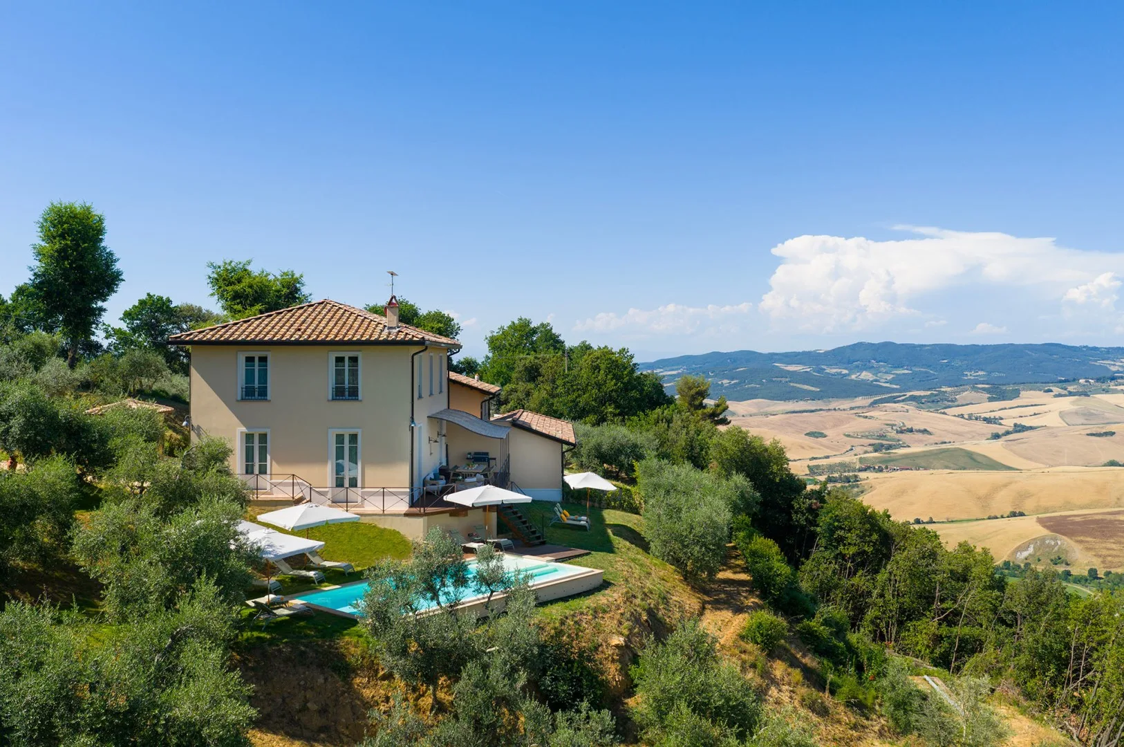 Una casa rural con piscina está rodeada de árboles y contempla campos ondulados.