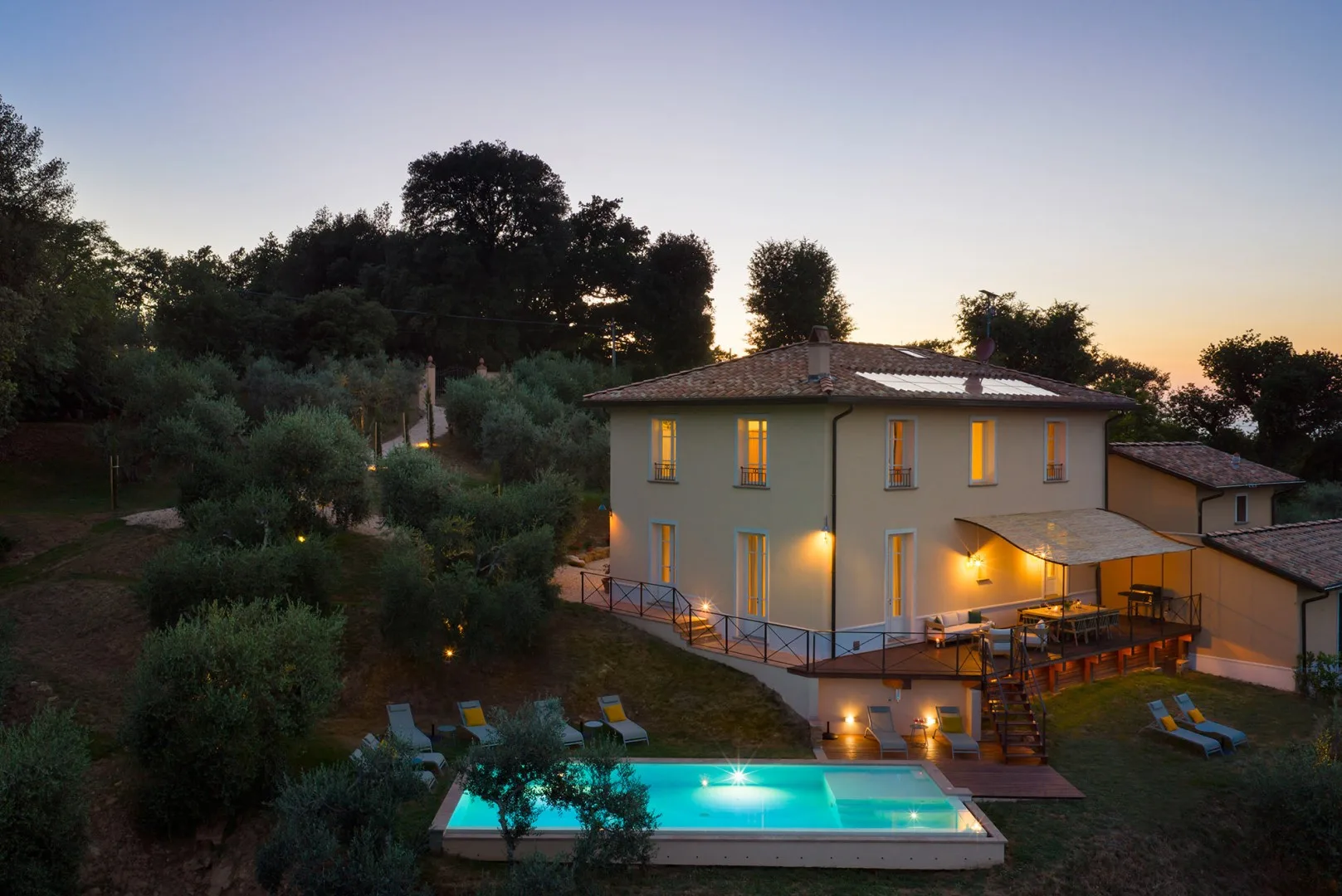 Una casa con piscina iluminada y asientos al aire libre al anochecer.