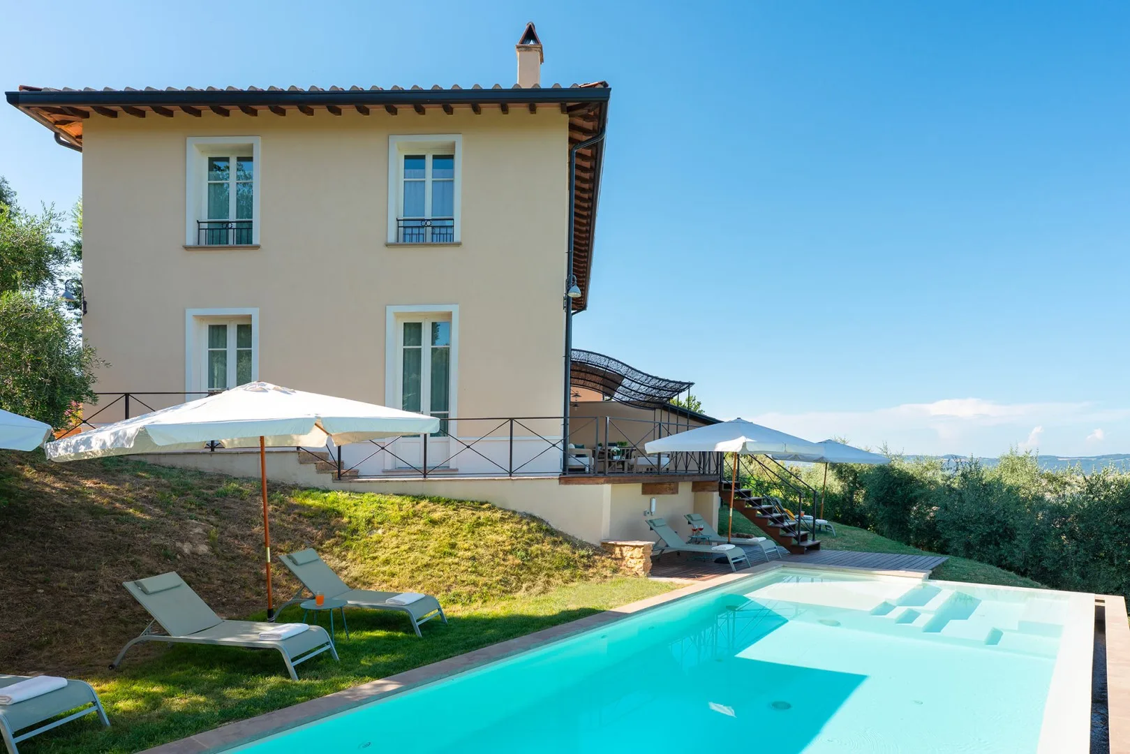 Una casa junto a una piscina, con asientos al aire libre y una terraza soleada.