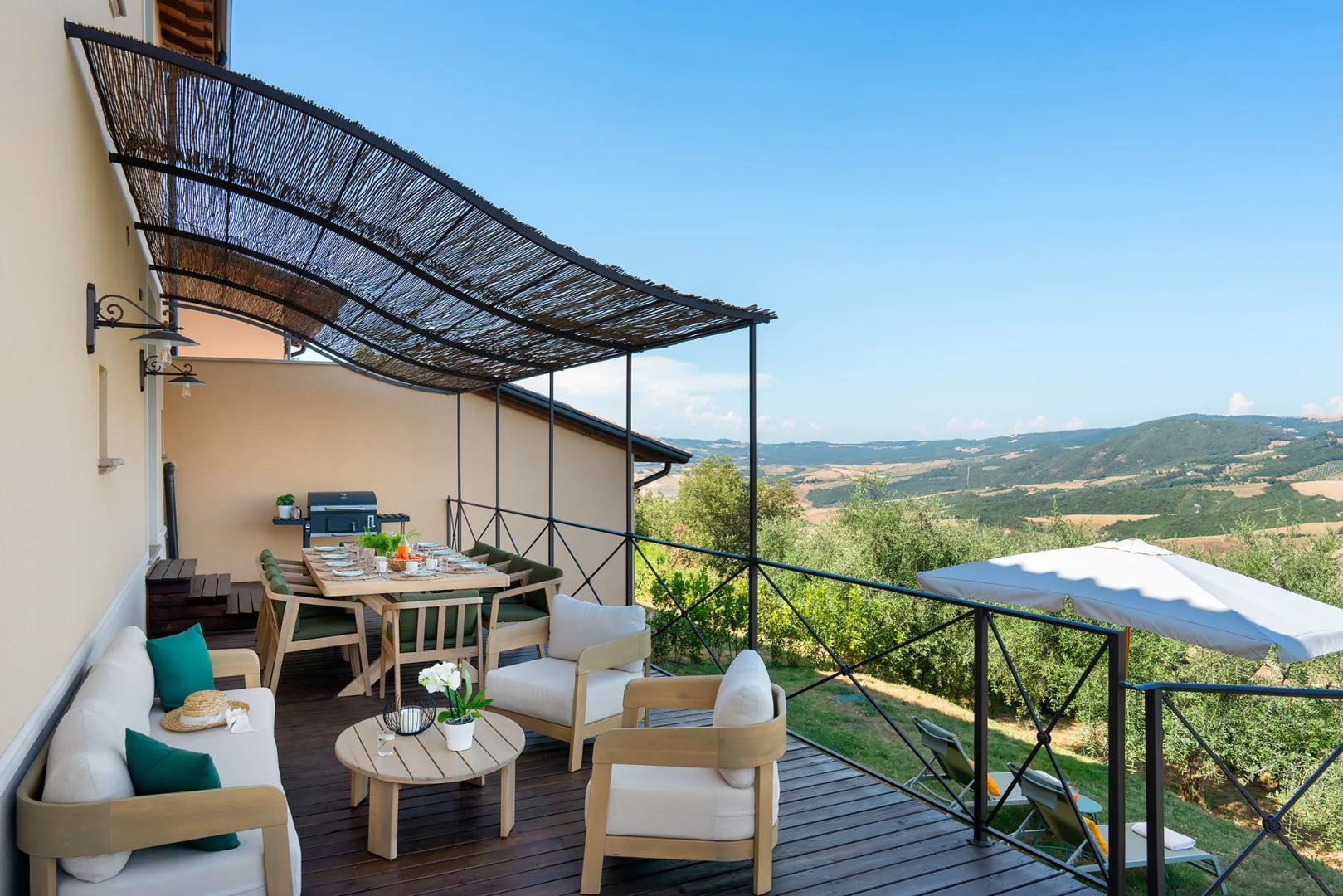 Una terraza al aire libre tiene asientos bajo un toldo tejido y vistas a colinas.