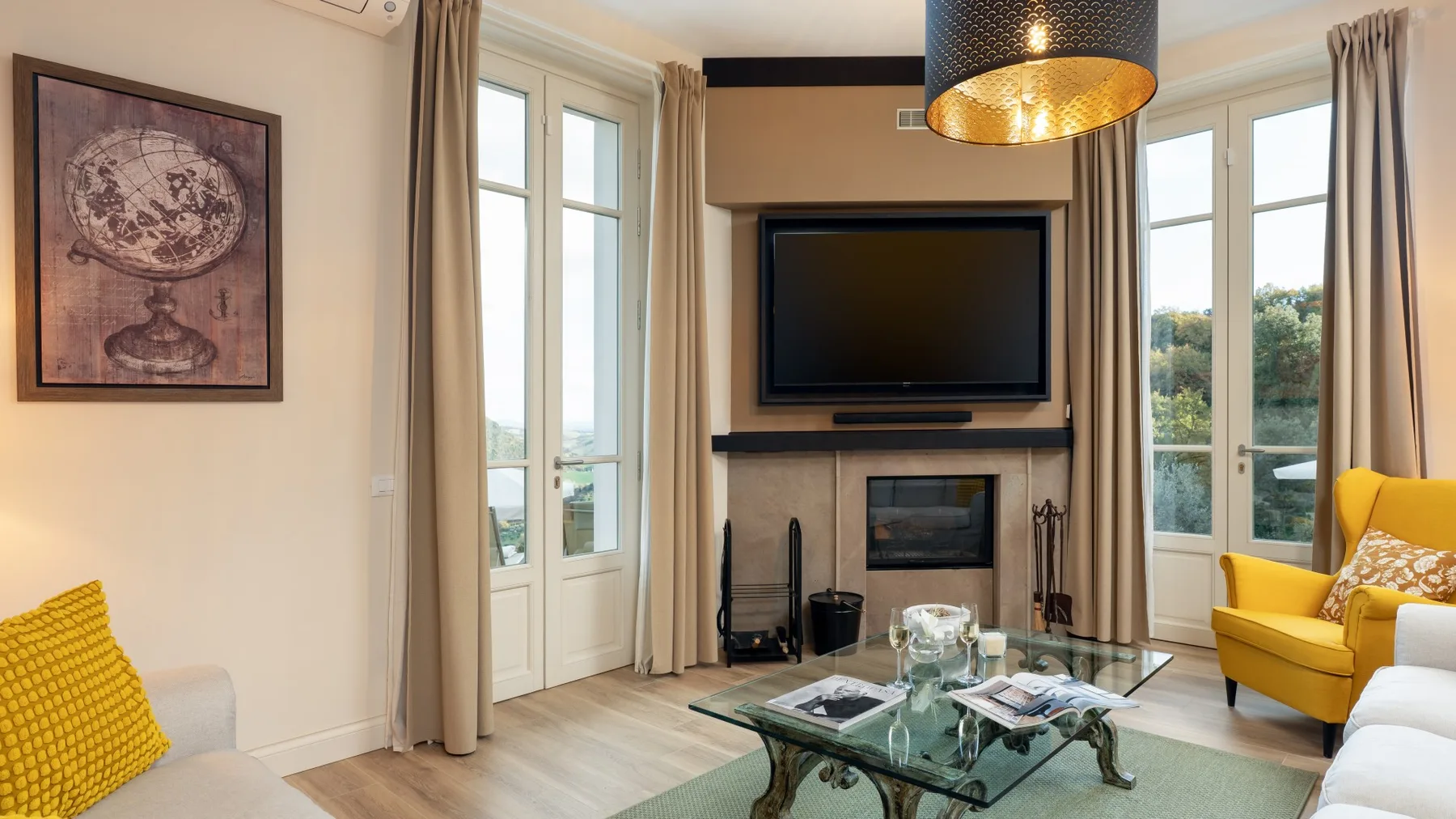 Una sala de estar con un televisor sobre una chimenea y asientos junto a ventanas altas.