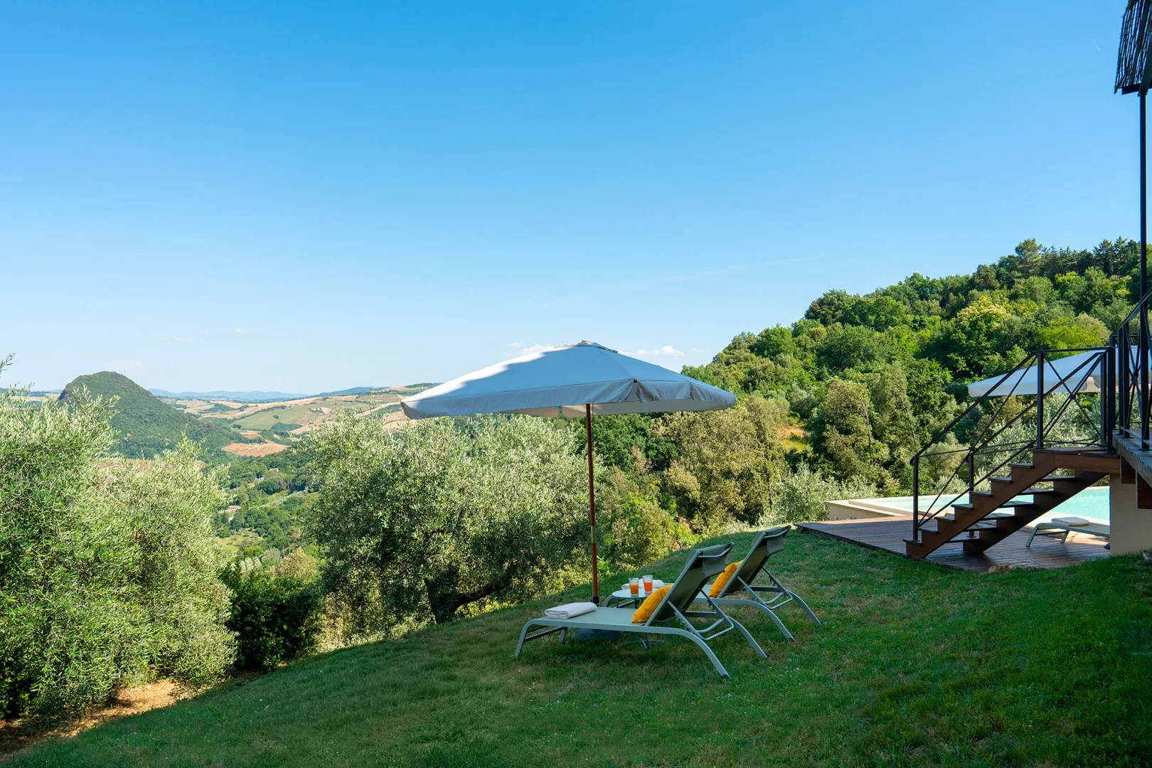 Un patio al aire libre con asientos y una sombrilla tiene vistas a una ladera verde.