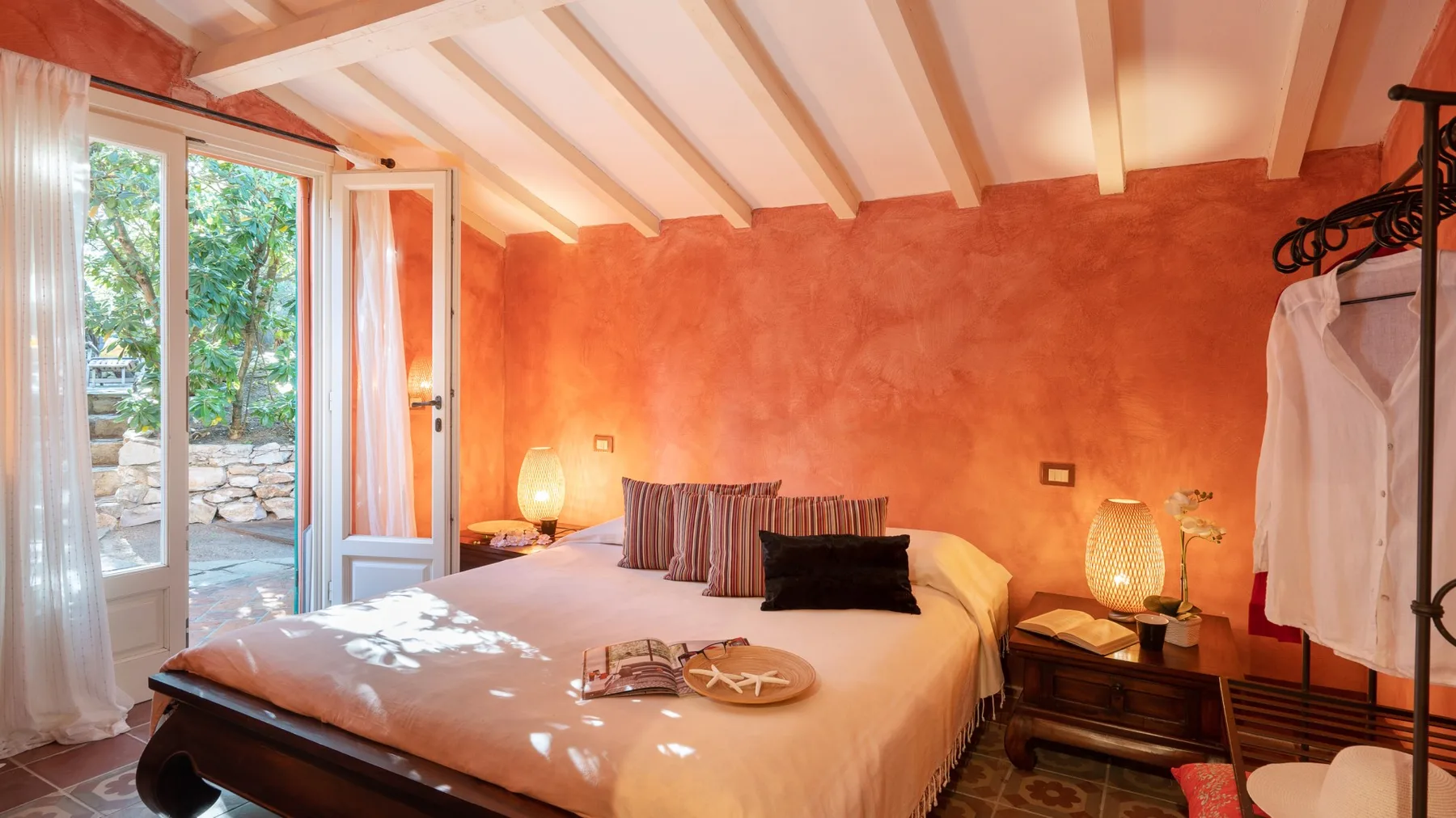 A bedroom with a bed, bedside tables, and an open glass door.