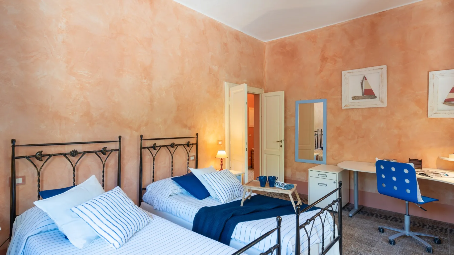A bedroom with two beds and a desk against peach-colored walls.