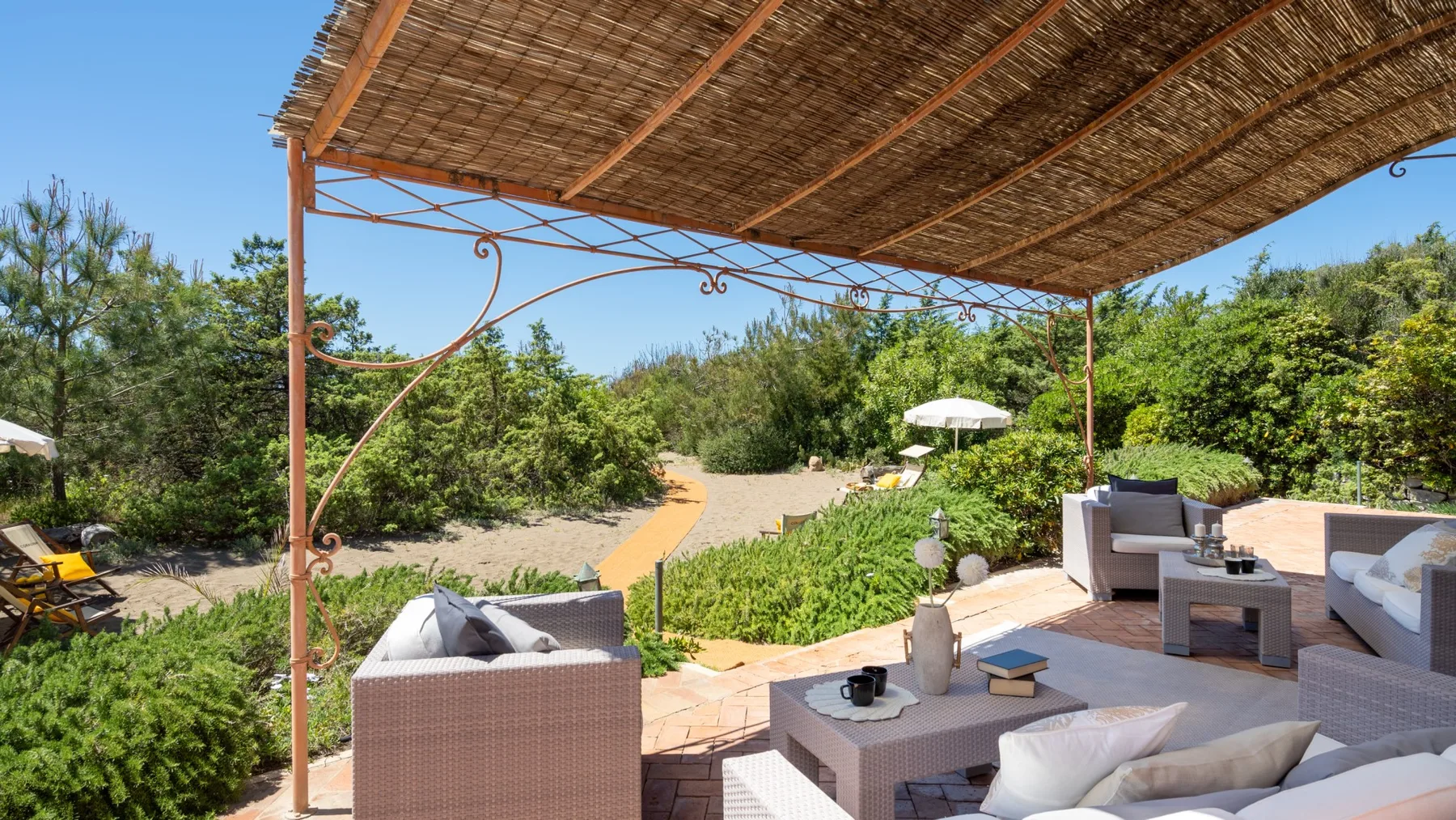 An outdoor patio with cushioned seating and a woven canopy overlooks a garden path.