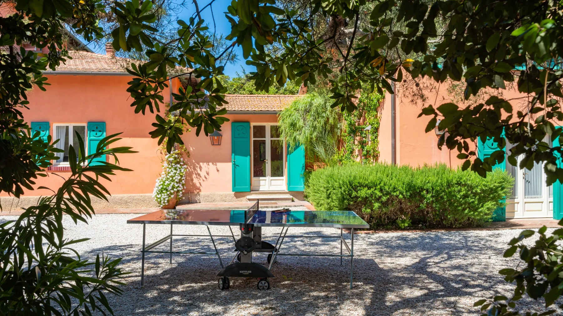 A peach-colored house with a ping-pong table on the shaded gravel patio.