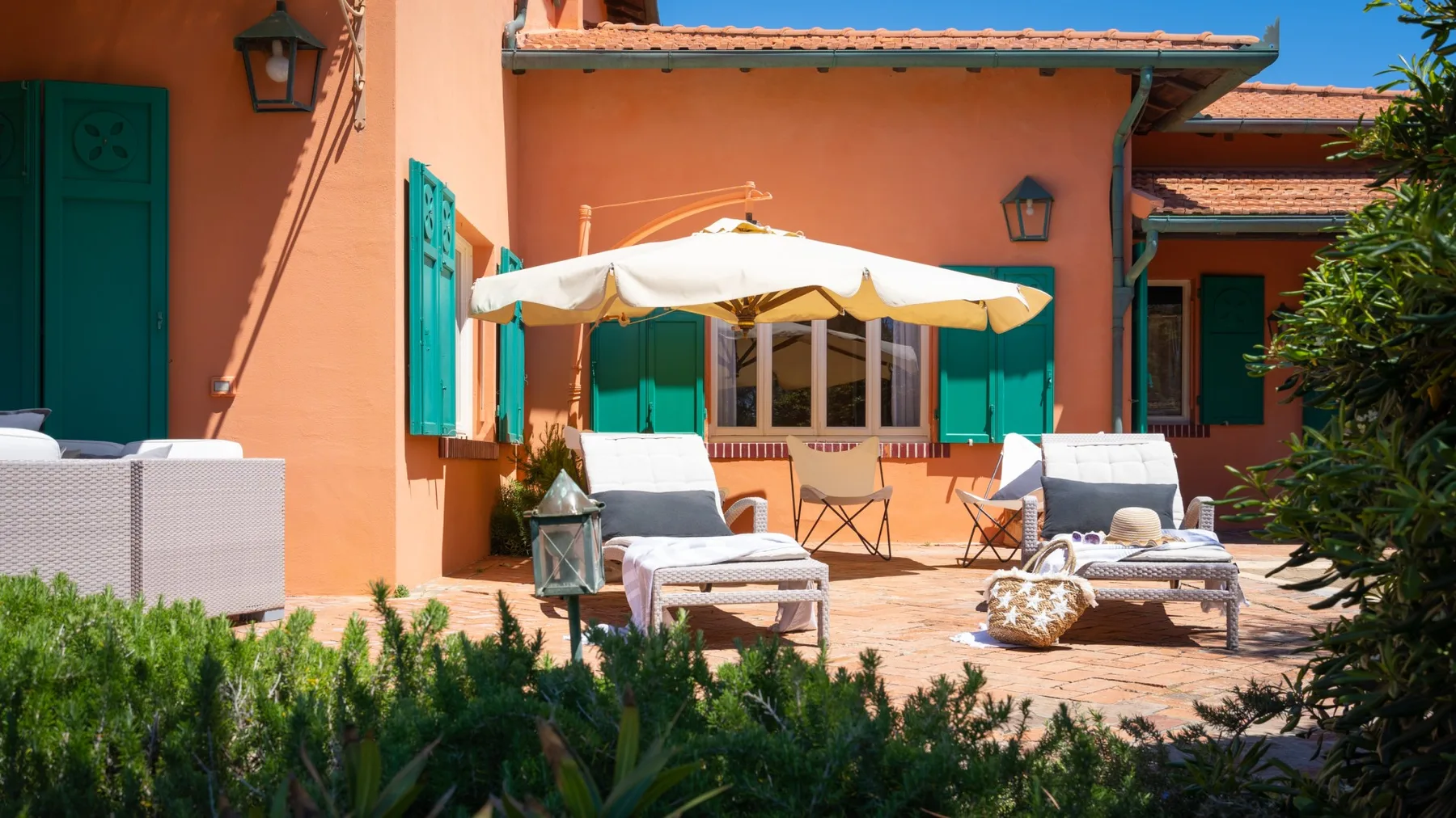 A sunny patio with outdoor seating, a large umbrella, and a peach-colored building.