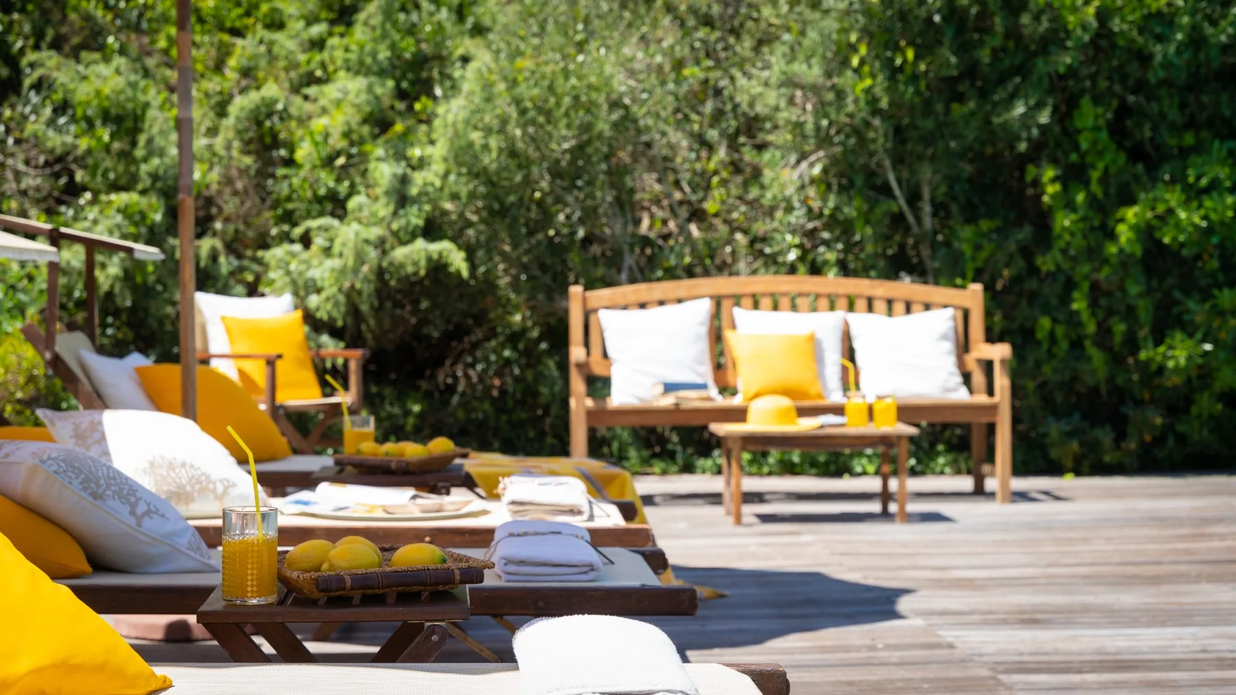 An outdoor lounge area with seating, cushions, and a low table on a wooden deck.