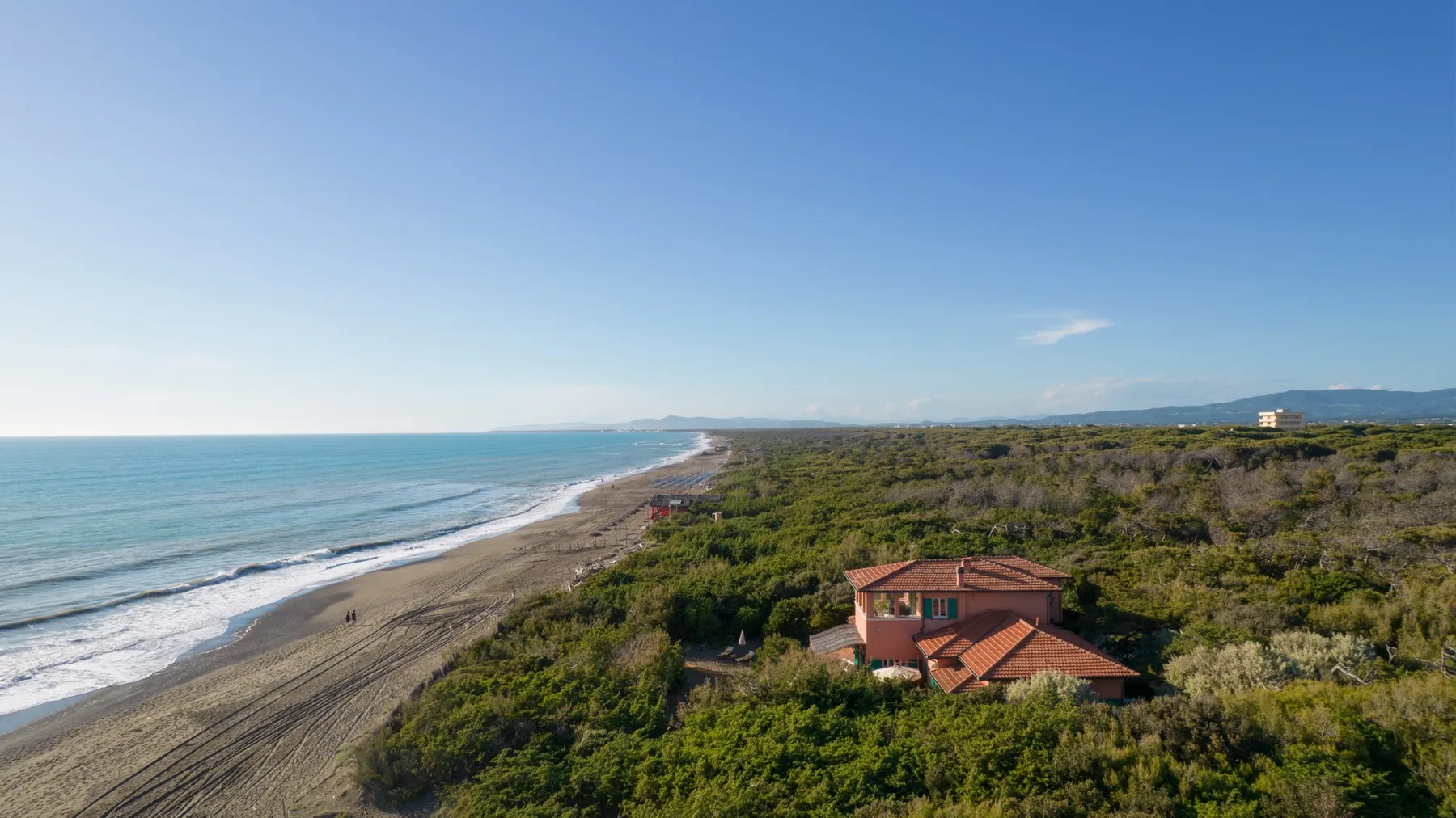 Aerial view of a red-roofed building amid coastal greenery beside the beach.