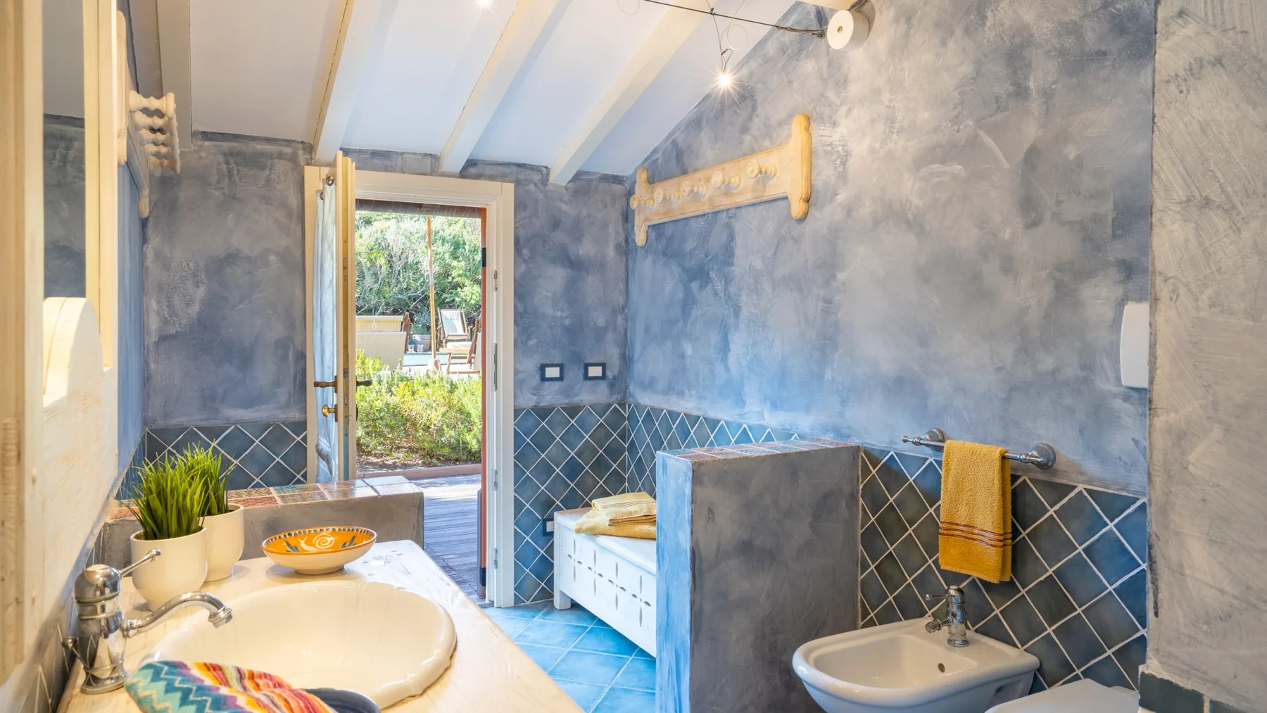 A bathroom with a sink, bidet, and blue-gray tiled walls.