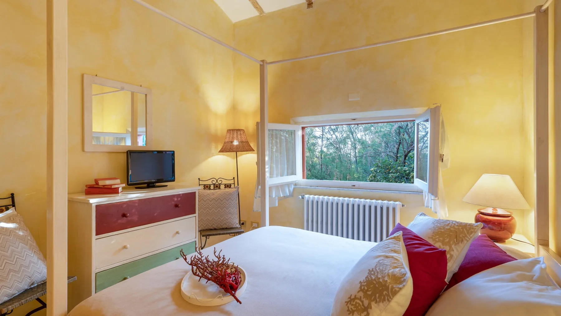 A bedroom with a bed, colorful pillows, and a window overlooking trees.