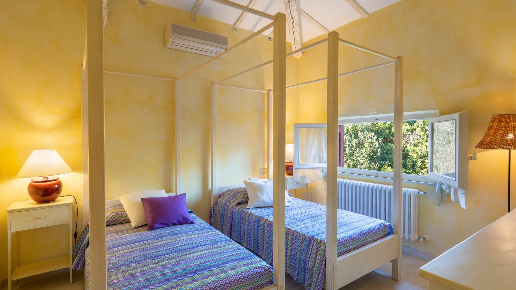 A bright bedroom with two beds, yellow walls, and an open window.