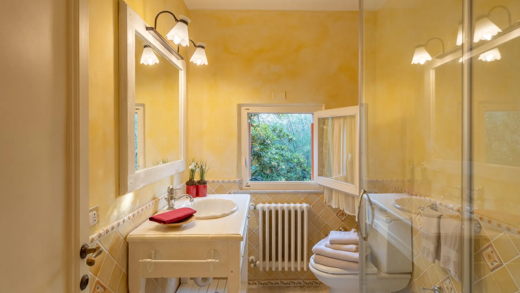 A yellow bathroom with a sink, toilet, and window overlooking greenery.