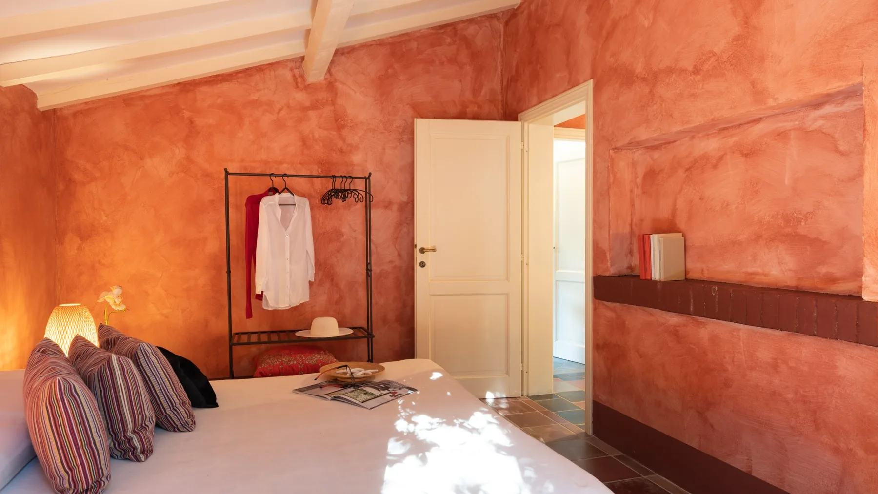 A bedroom with a bed, open clothing rack, and open doorway.