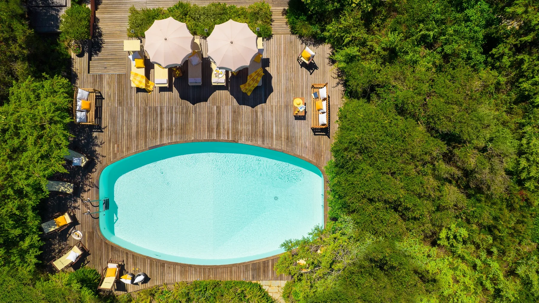 An outdoor swimming pool sits beside a wooden deck with seating and umbrellas.