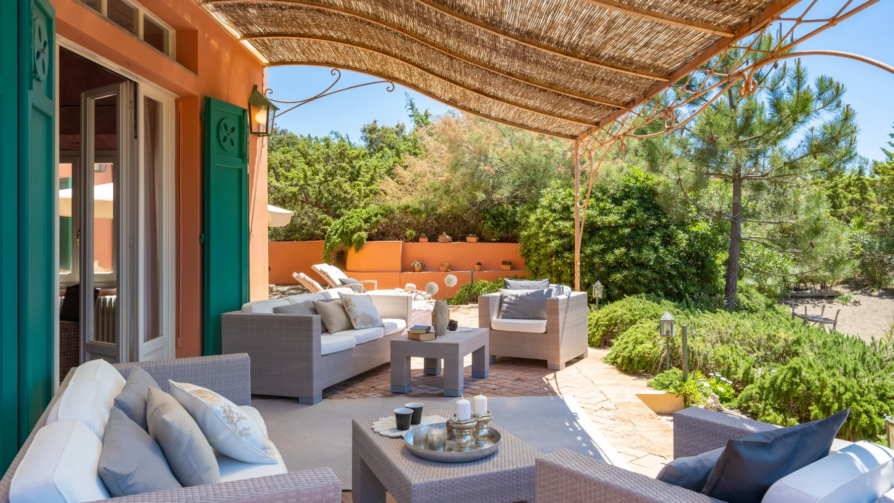 A covered outdoor seating area with cushioned furniture and surrounding greenery.