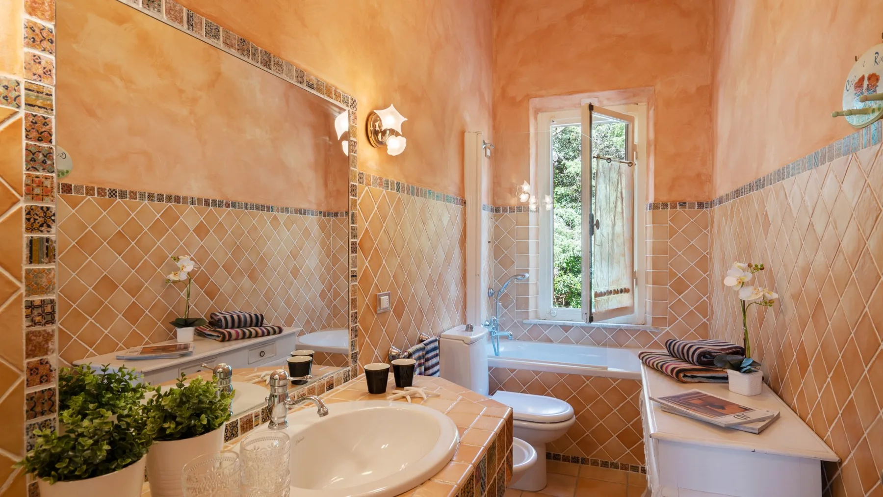 A warm-toned bathroom with a sink and a window above the bathtub.