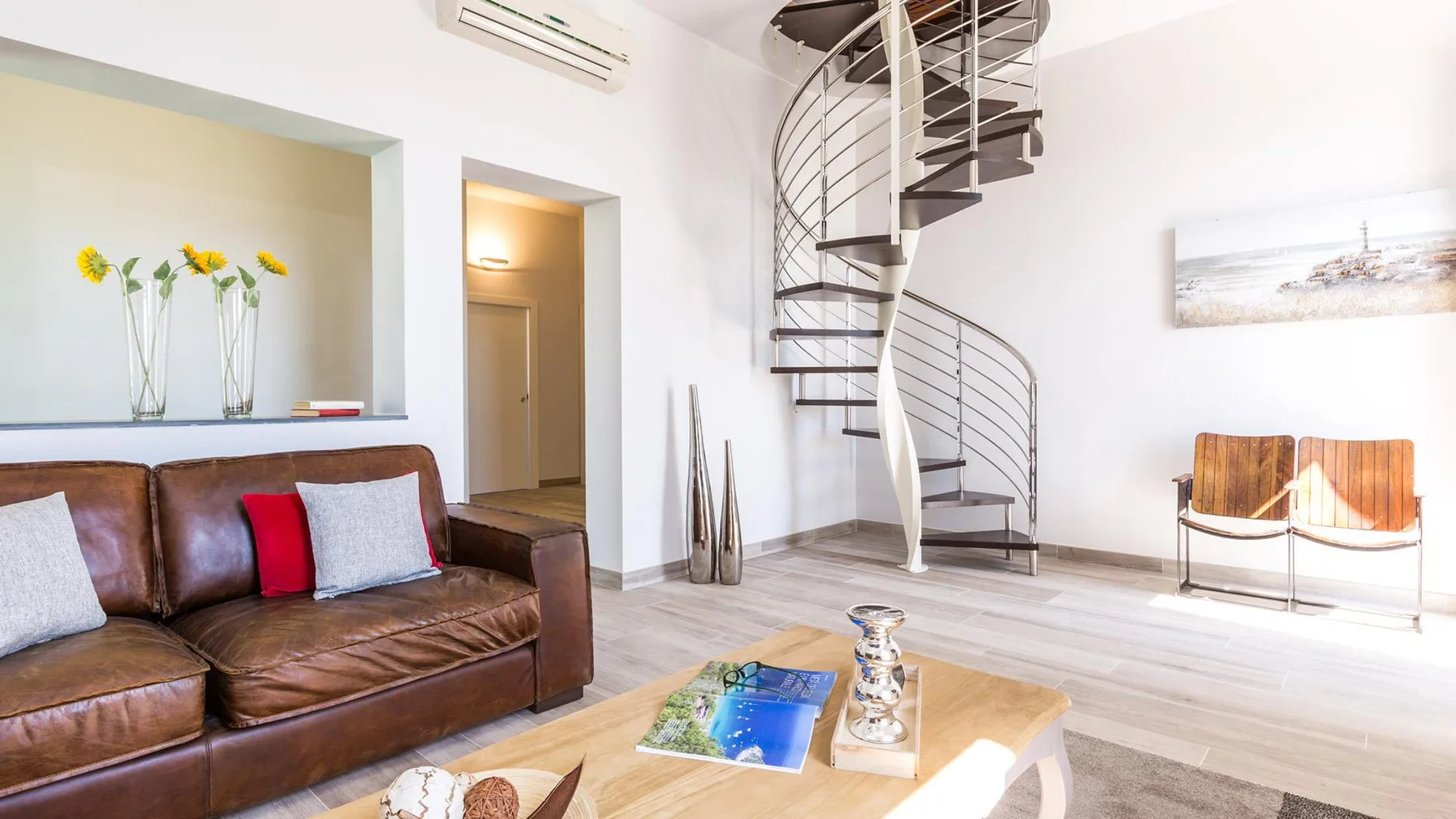 A bright living room with brown seating and a spiral staircase.