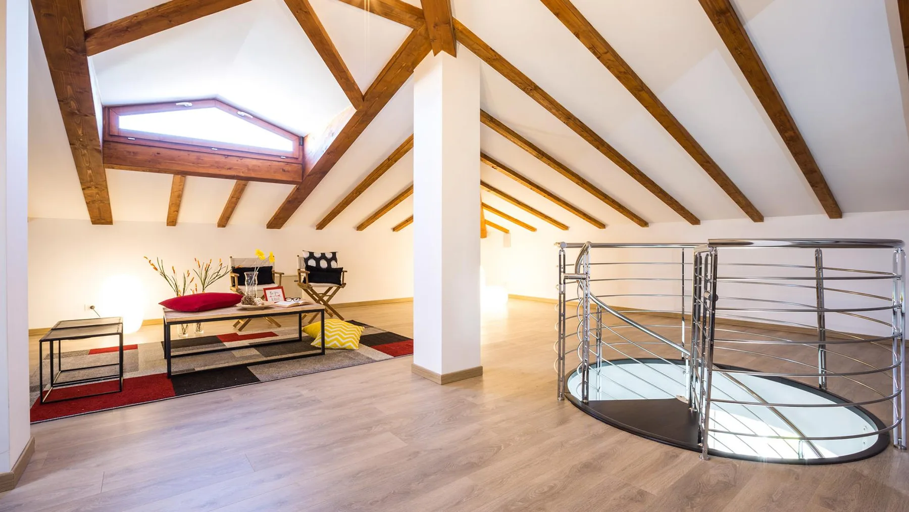 An attic lounge with exposed wooden beams, low seating, and a metal railing around an opening.