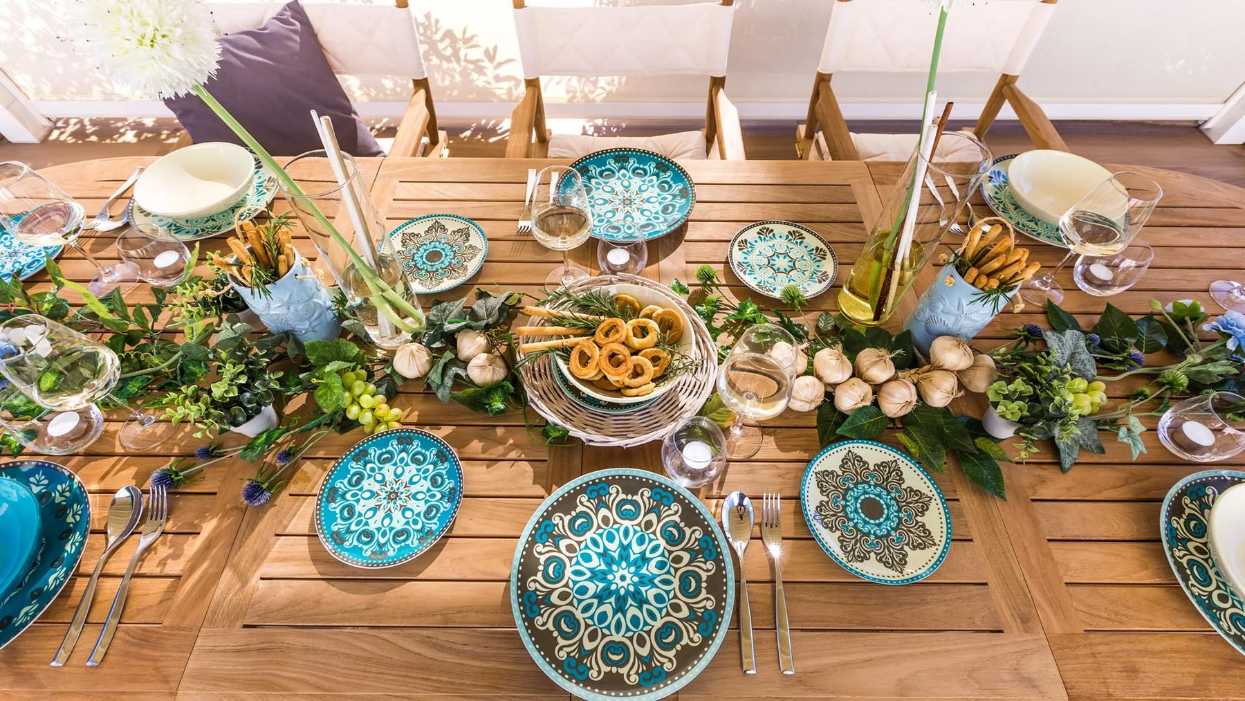 A long dining table is set with patterned plates and a green centerpiece.