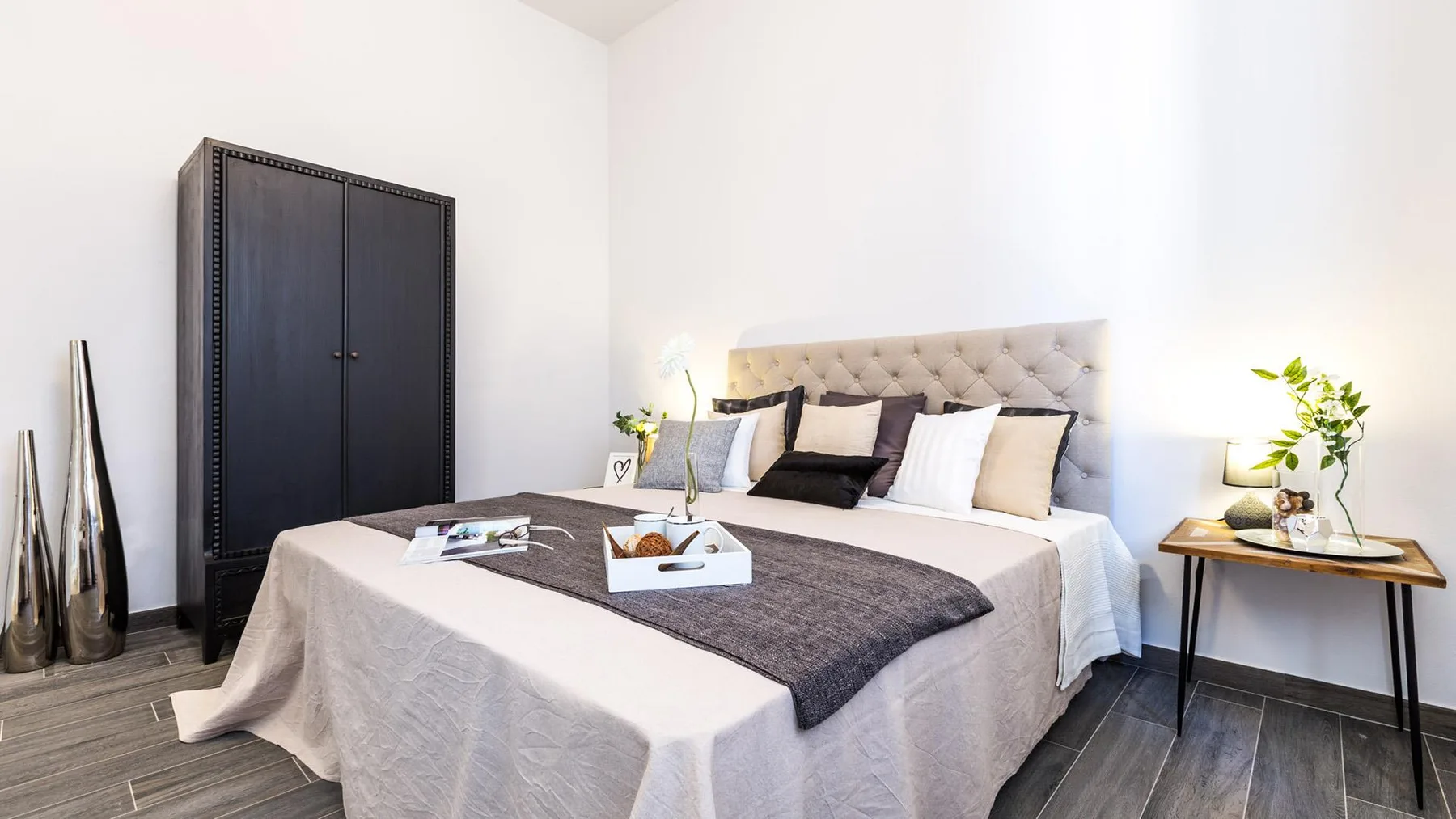 A bedroom with a large bed, dark wardrobe, and bedside tables.