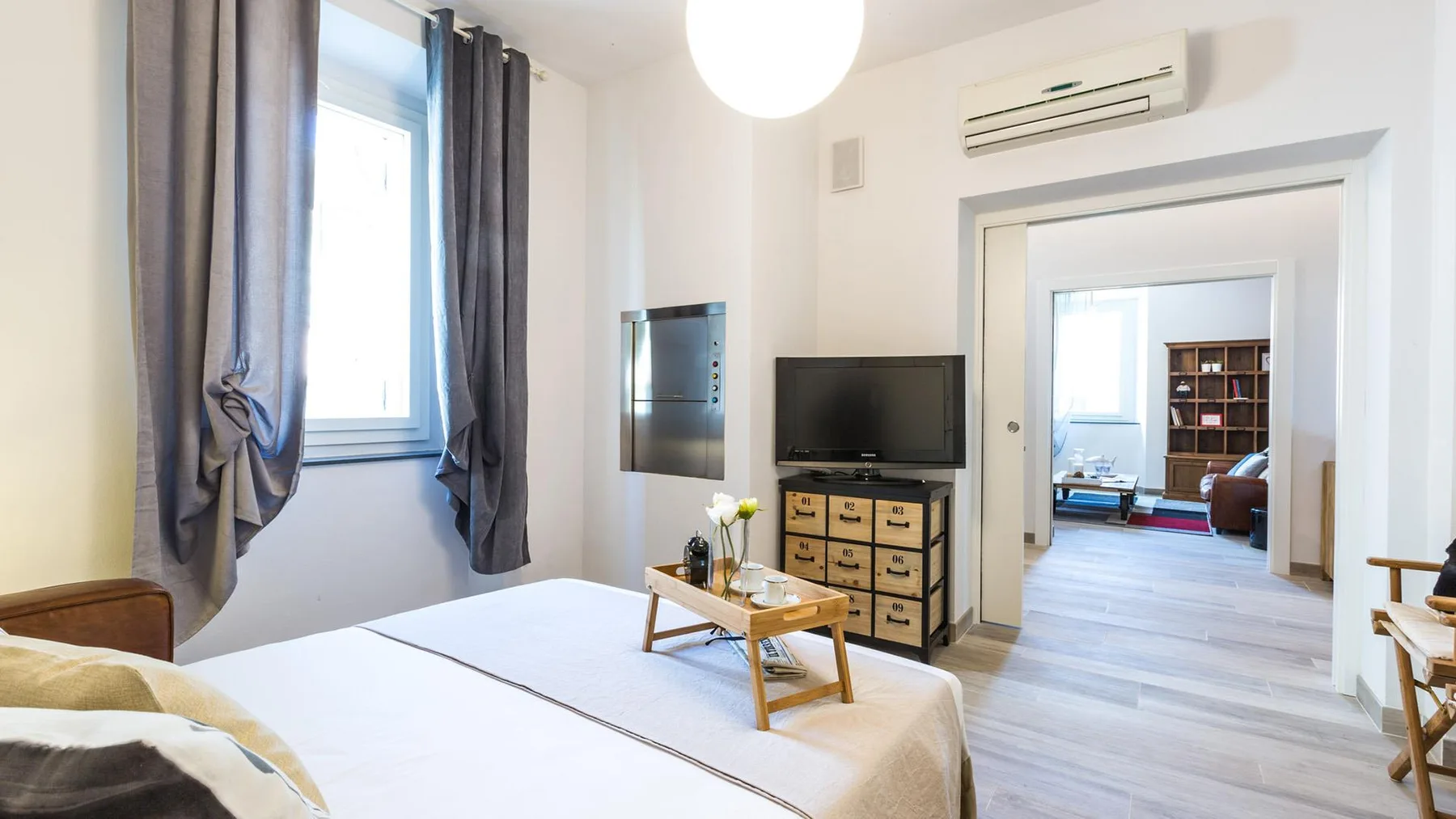 A bright bedroom with a large bed, a television, and an open doorway to another room.