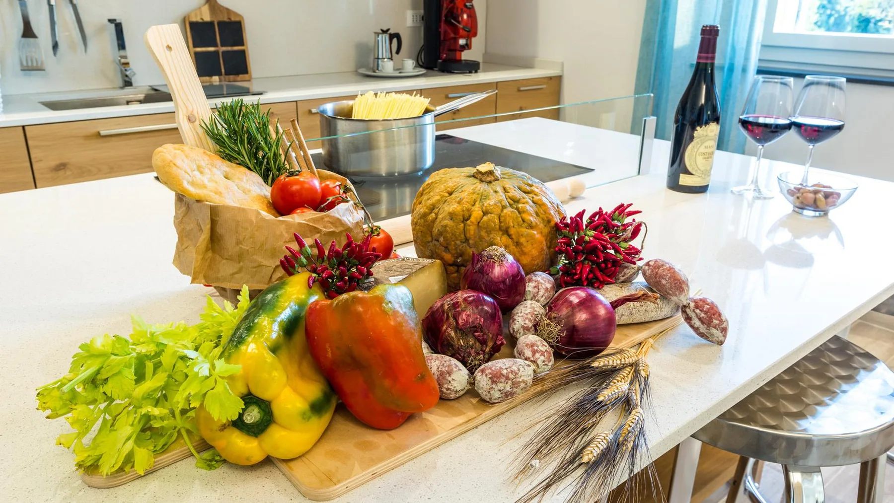 A bright kitchen counter displays fresh vegetables, bread, and a pot.
