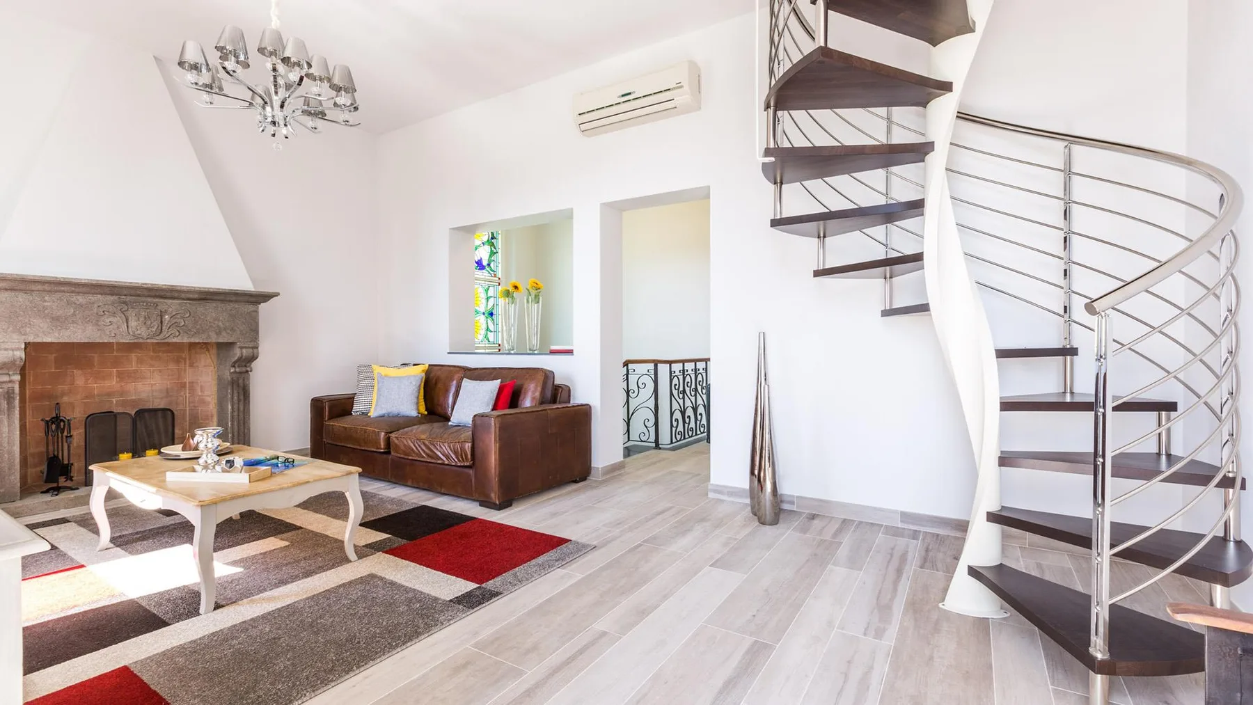 A bright living room with a seating area, fireplace, and spiral staircase.