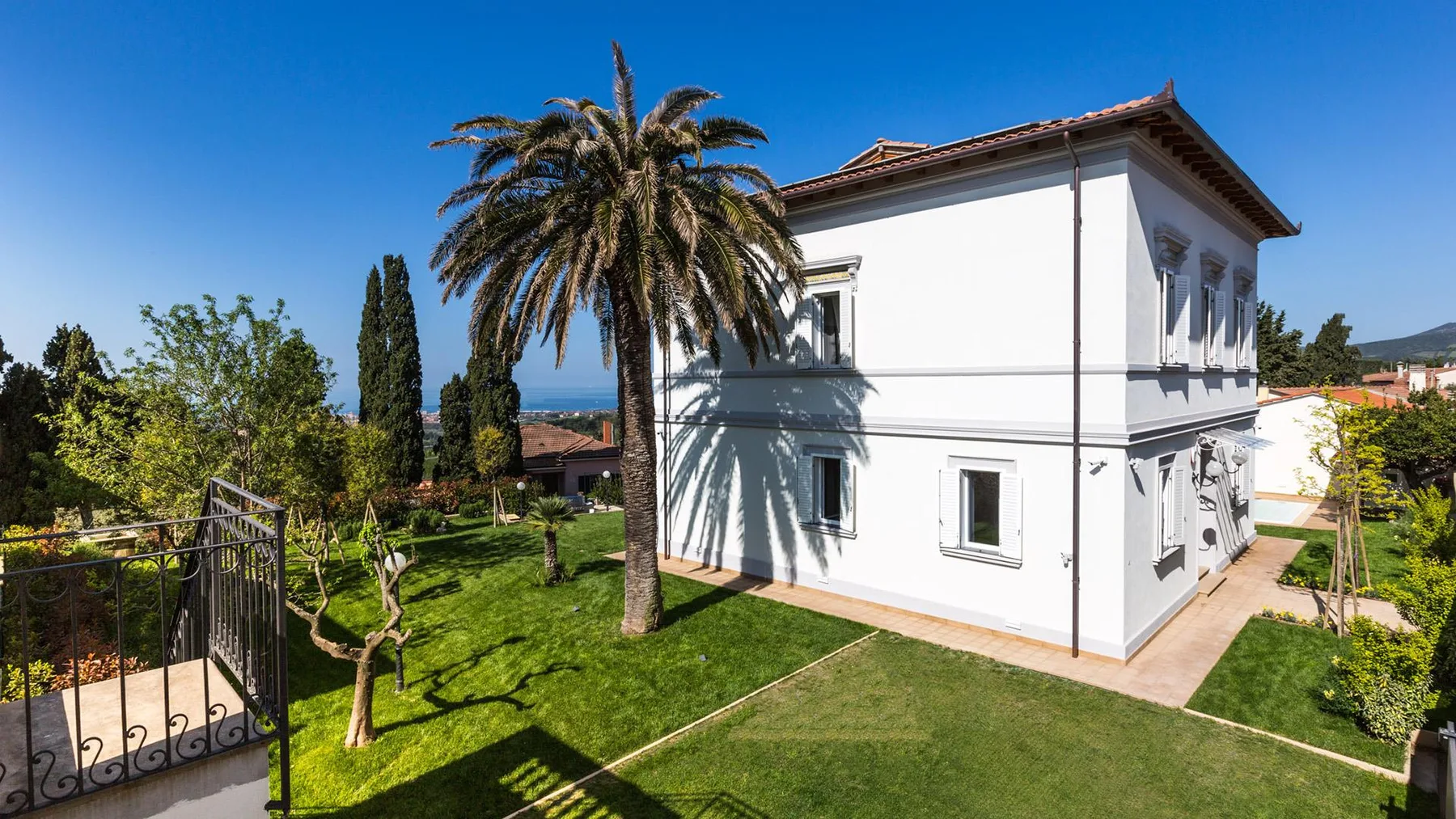 A white two-story house stands beside a palm tree and green lawn.