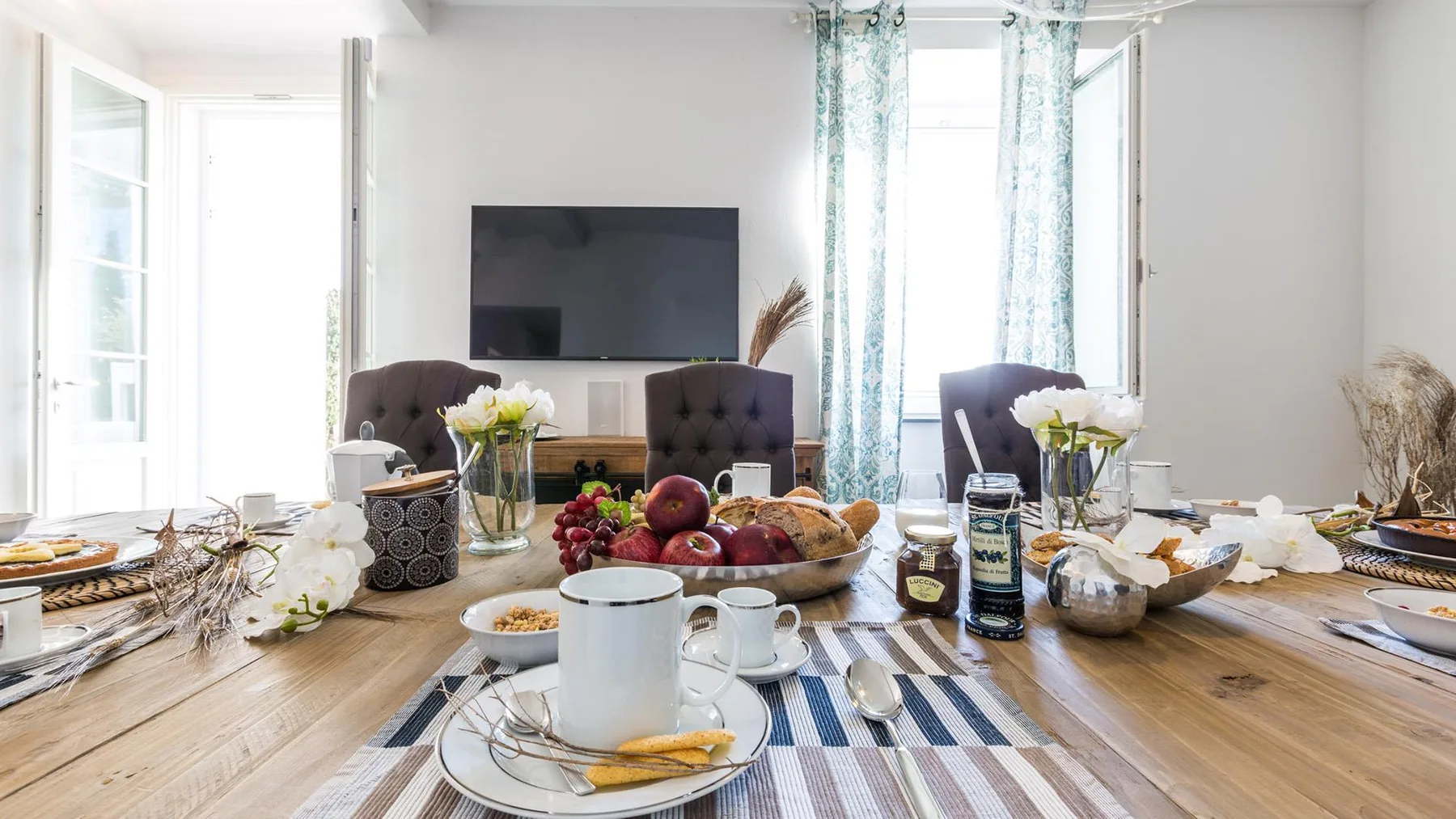 A bright dining area with a set table and a television on the wall.