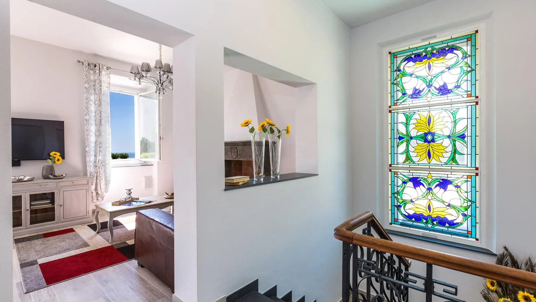 A bright living room with a colorful stained-glass window beside the seating area.