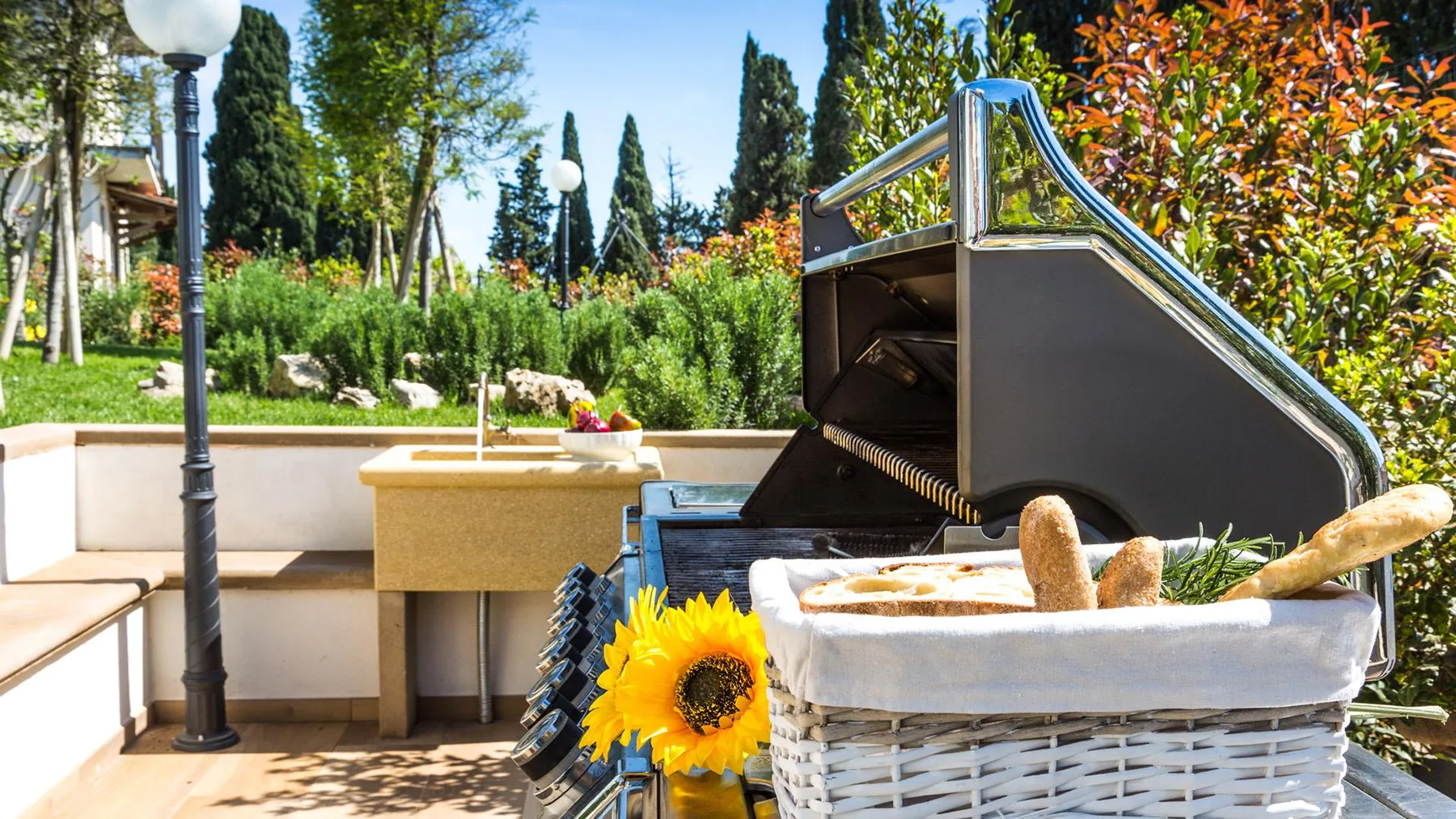 An outdoor counter and cooking area sit beside a basket of bread and flowers.