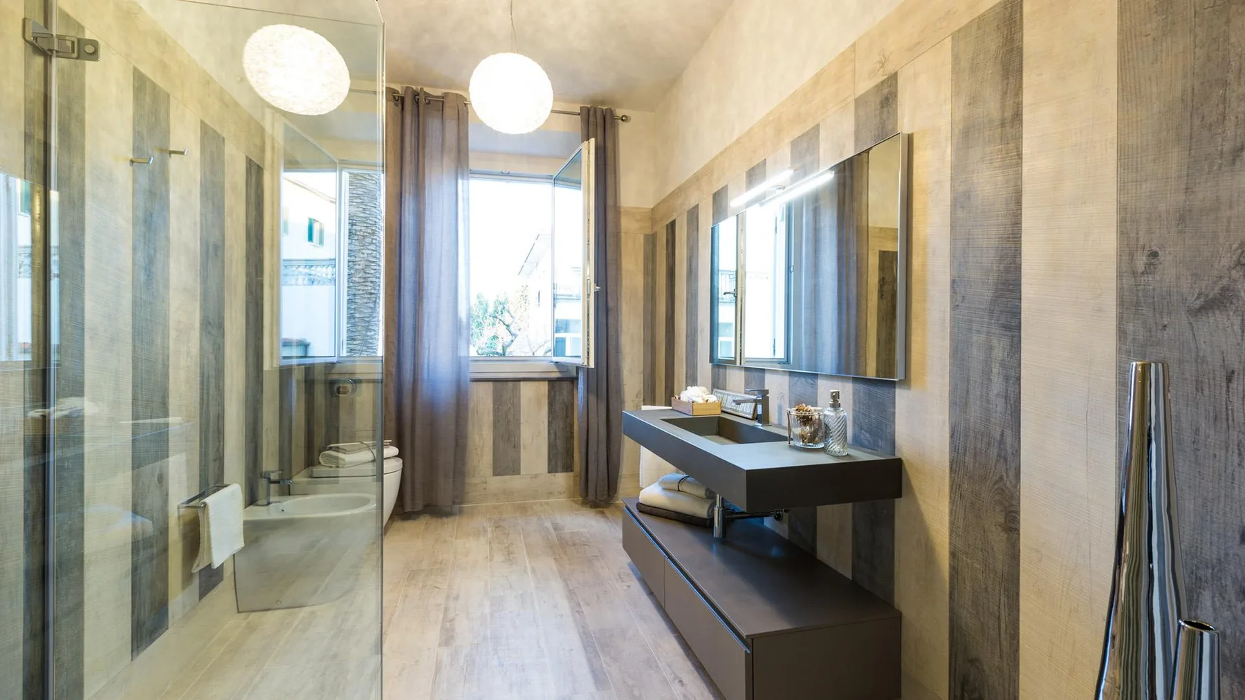 A bathroom with a glass shower and a dark vanity beneath a wide mirror.