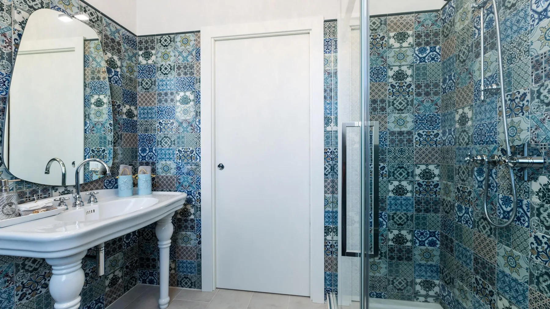 A bathroom with a pedestal sink, patterned tile walls, and a glass shower.