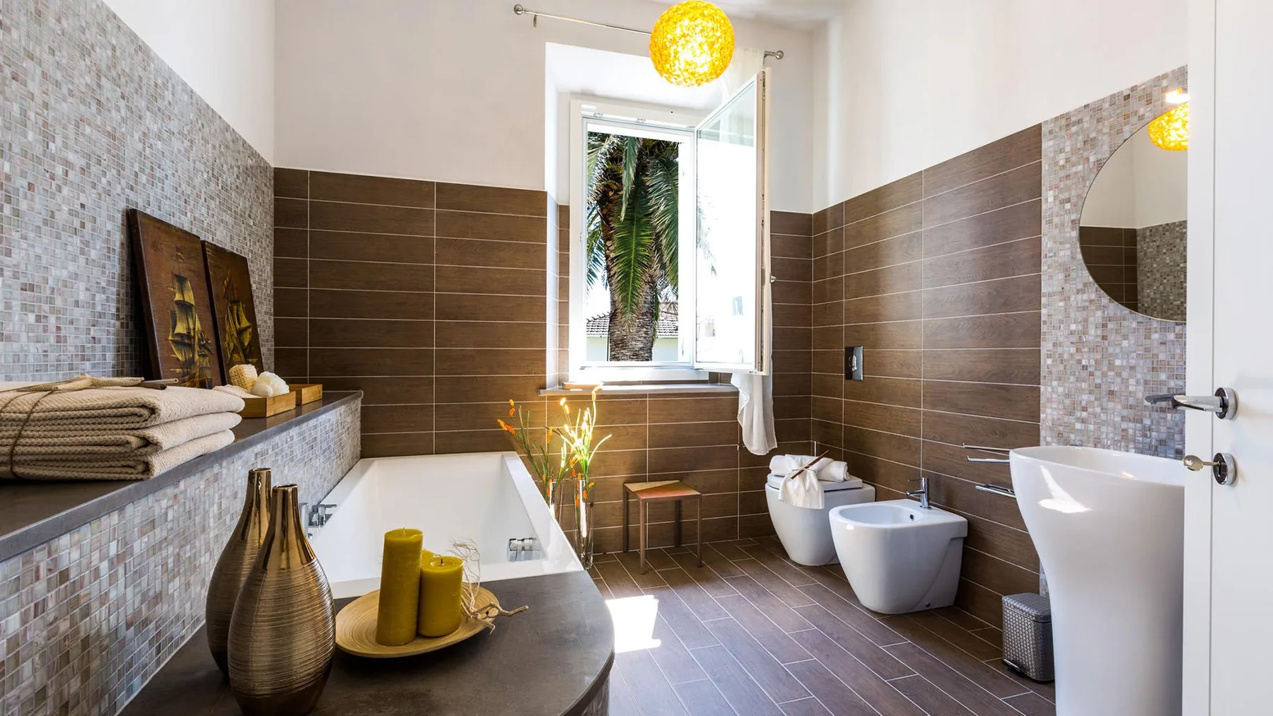 A tiled bathroom with a bathtub, sink, and window overlooking greenery.