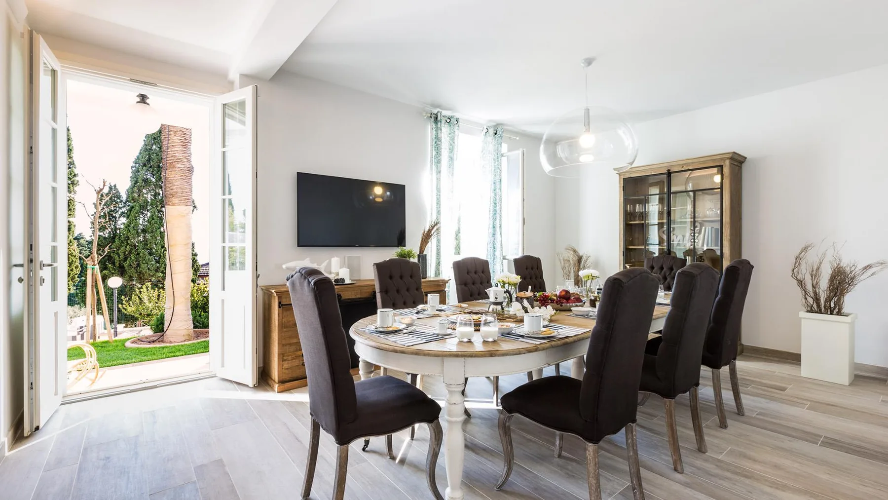 A dining room with a set table and tall dark seating beside open garden doors.