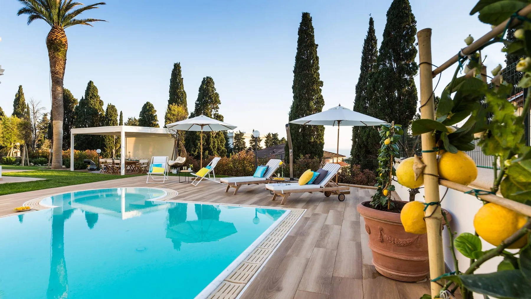 An outdoor swimming pool beside a tiled deck, lounge seating, and potted plants.