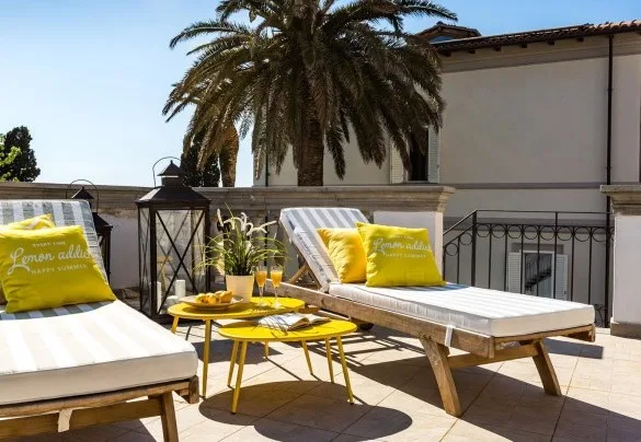 A sunny outdoor terrace with cushioned lounge seating and yellow accent pillows.