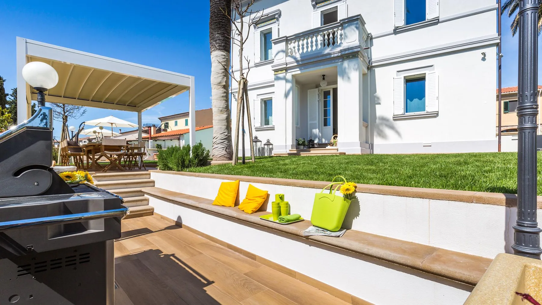 A sunny outdoor patio has a covered seating area and a grill.