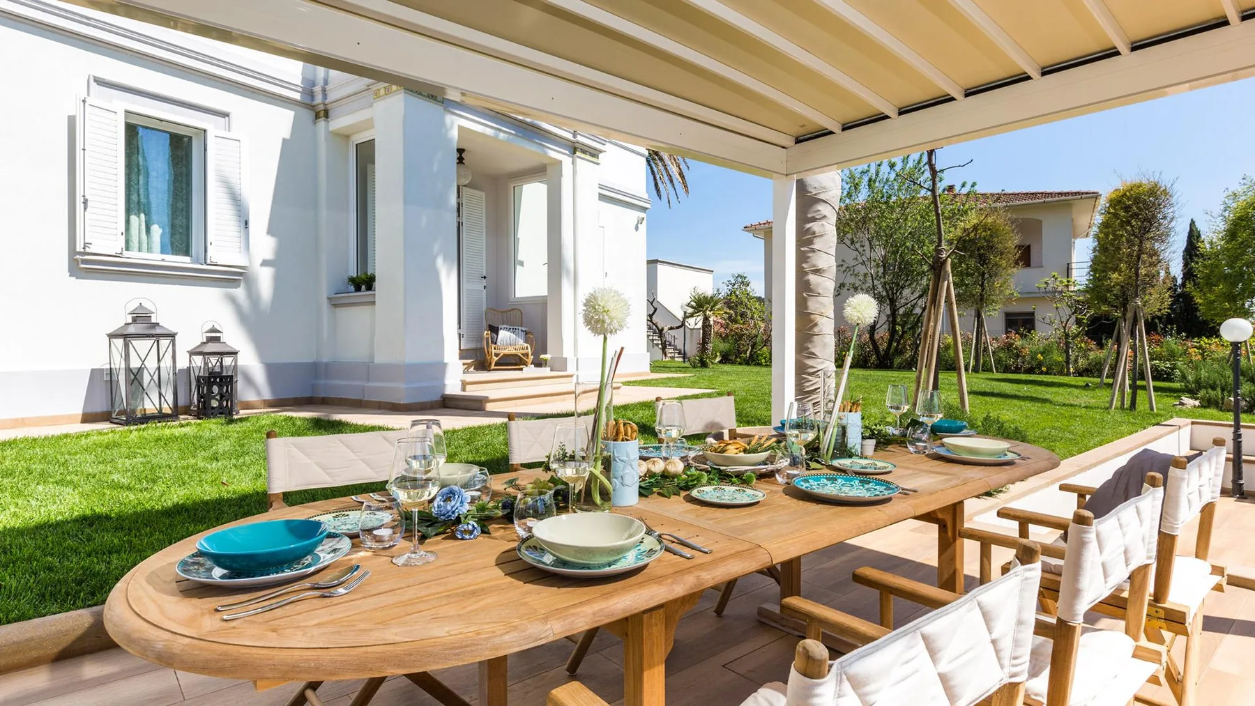An outdoor dining table sits on a covered patio beside a green lawn.