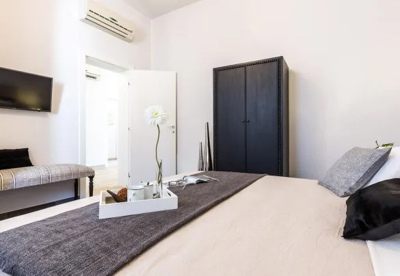 A bedroom with a bed, a dark wardrobe, and a television mounted on the wall.