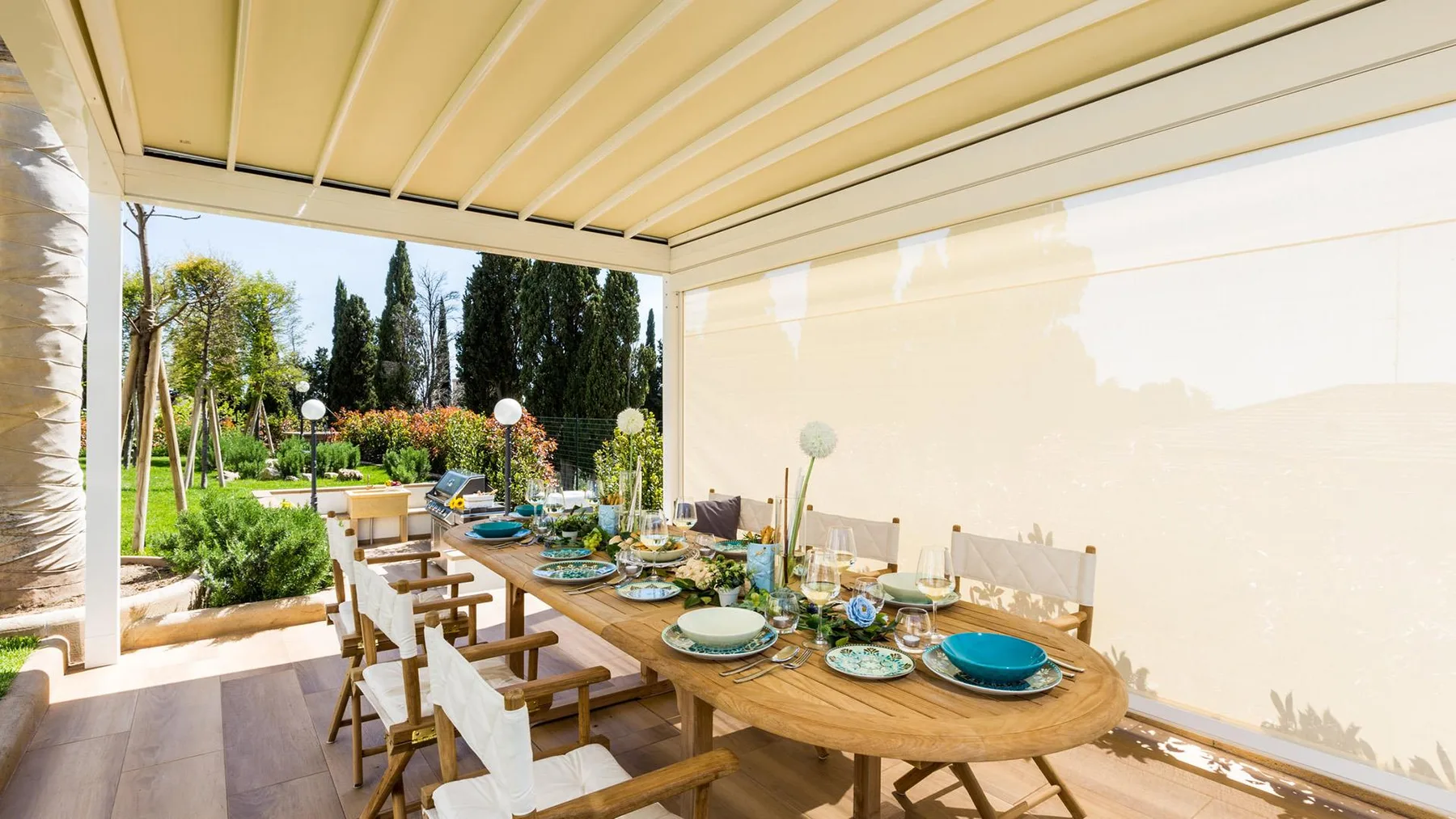 An outdoor dining area with a long table set beneath a covered patio.