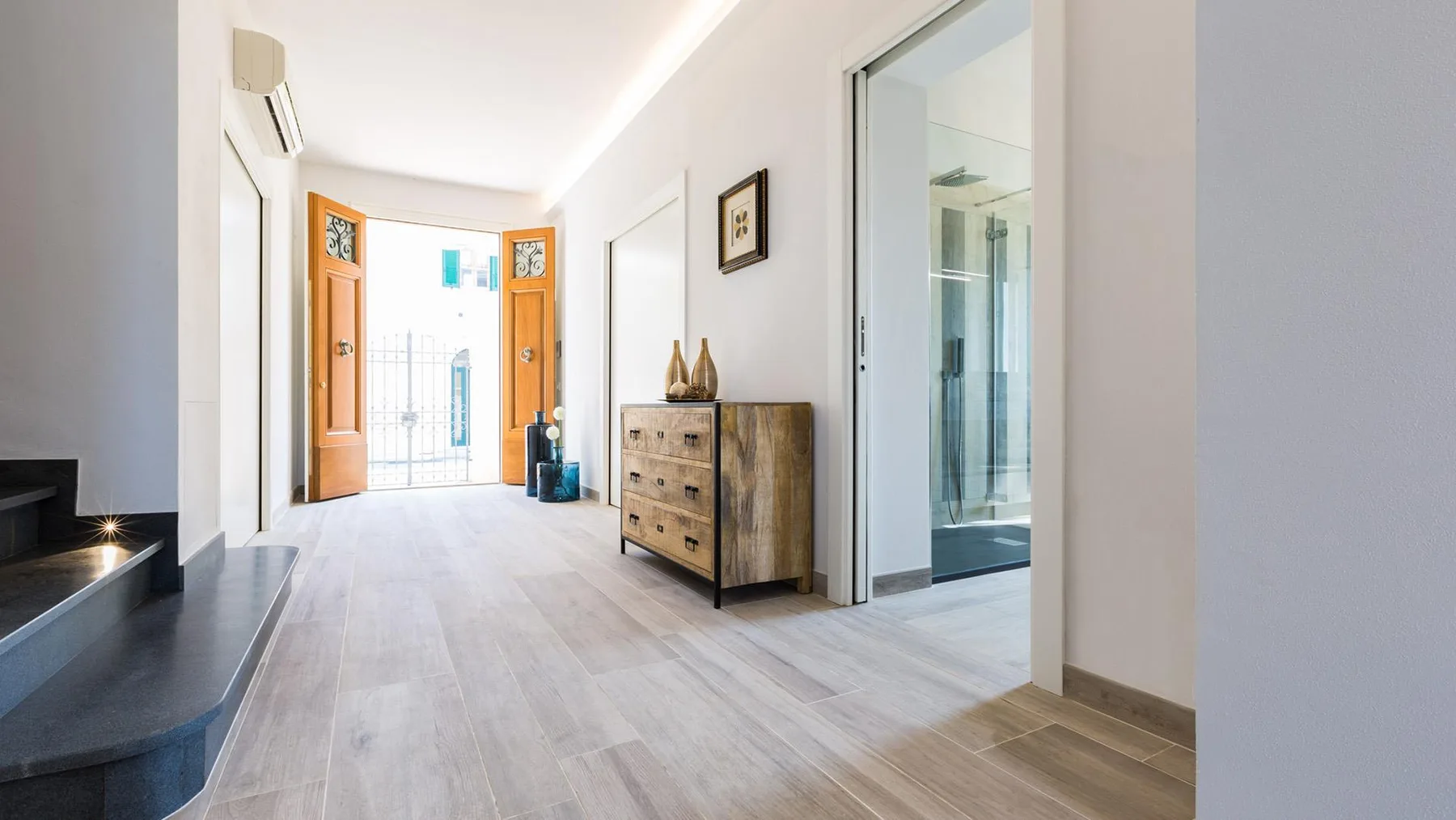A bright entry hall with open wooden doors and a chest of drawers.