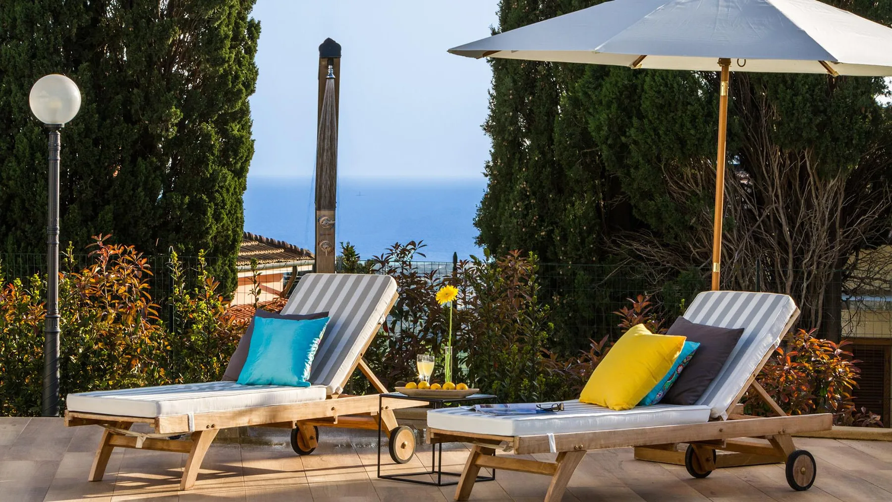 A patio with two lounge chairs and a large umbrella overlooks the sea.